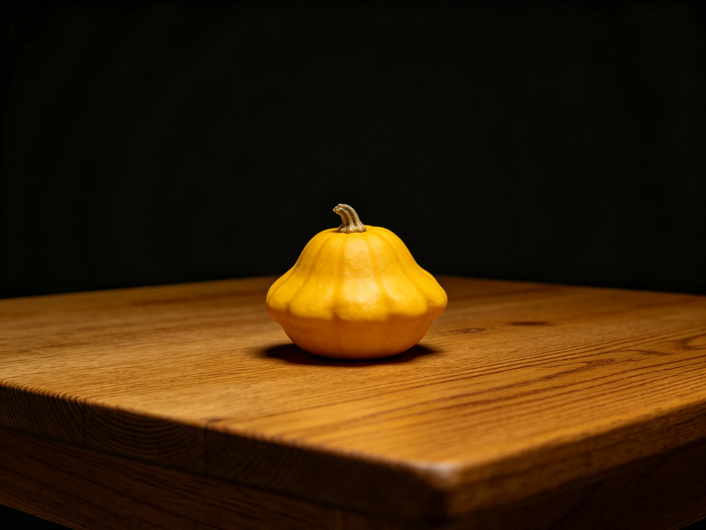 A single yellow squash rests on a polished wooden table with a dark backdrop.