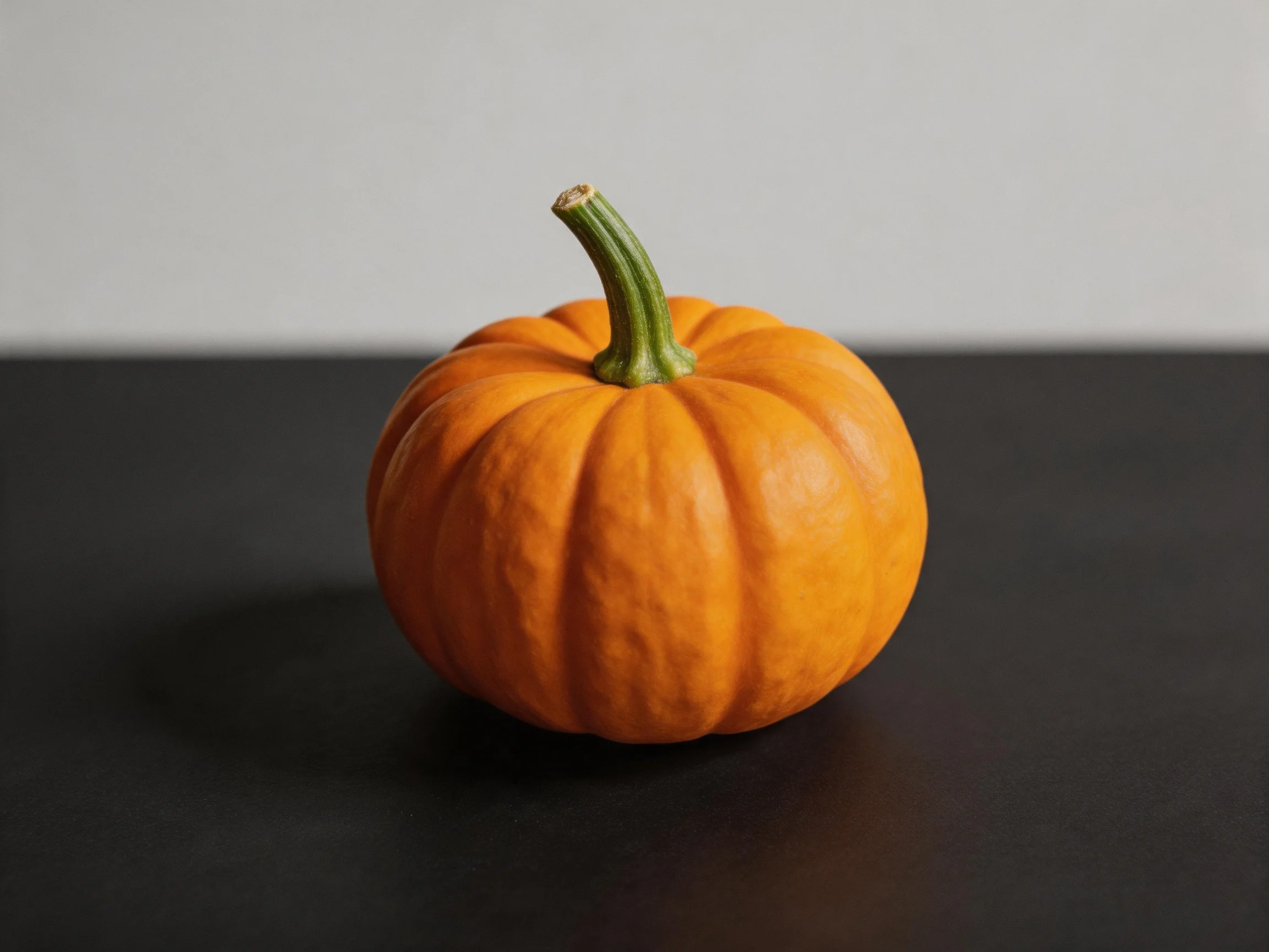 A small orange pumpkin with green stem on a dark surface