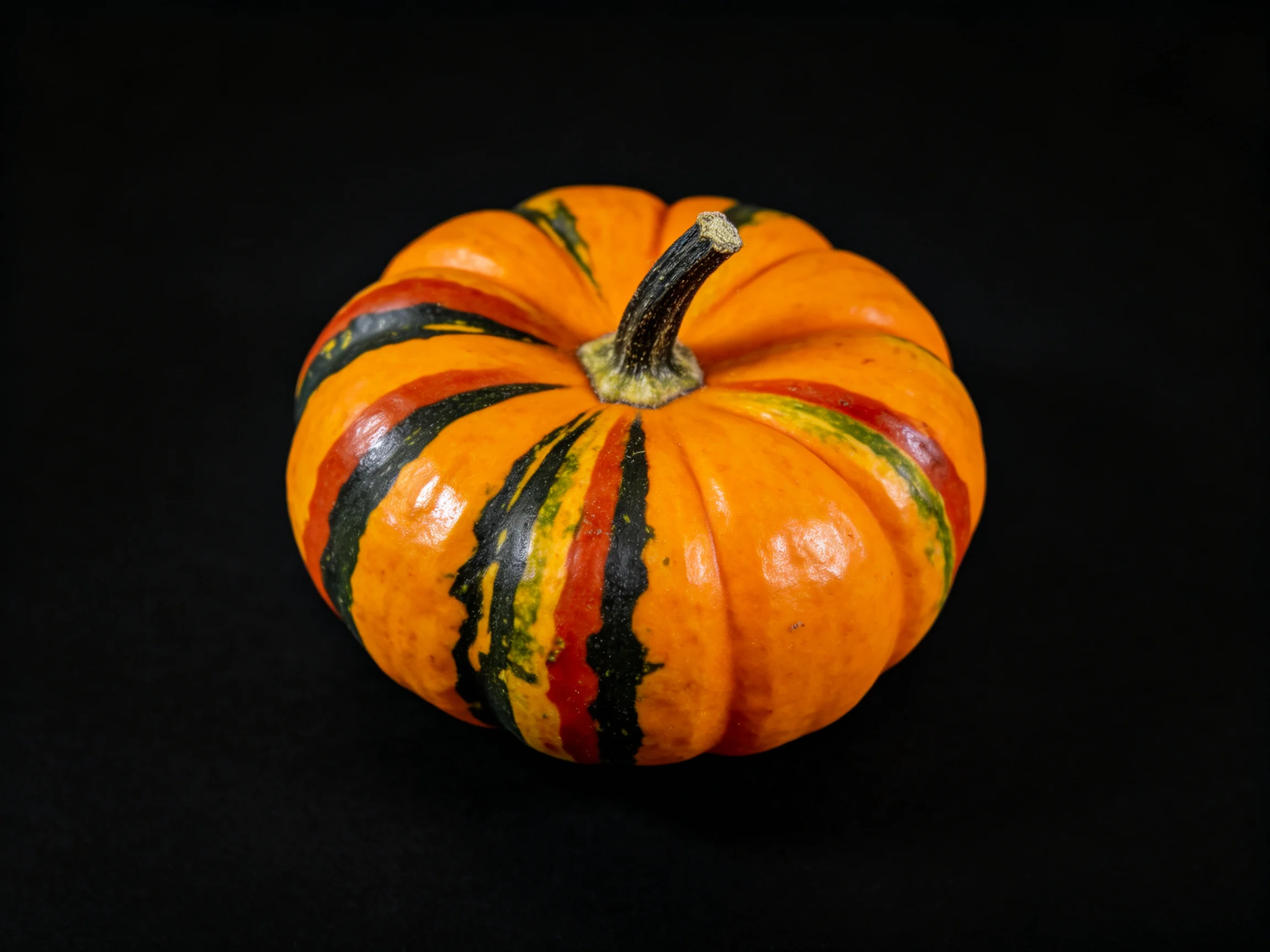 A small striped pumpkin with vibrant orange, black, and red markings
