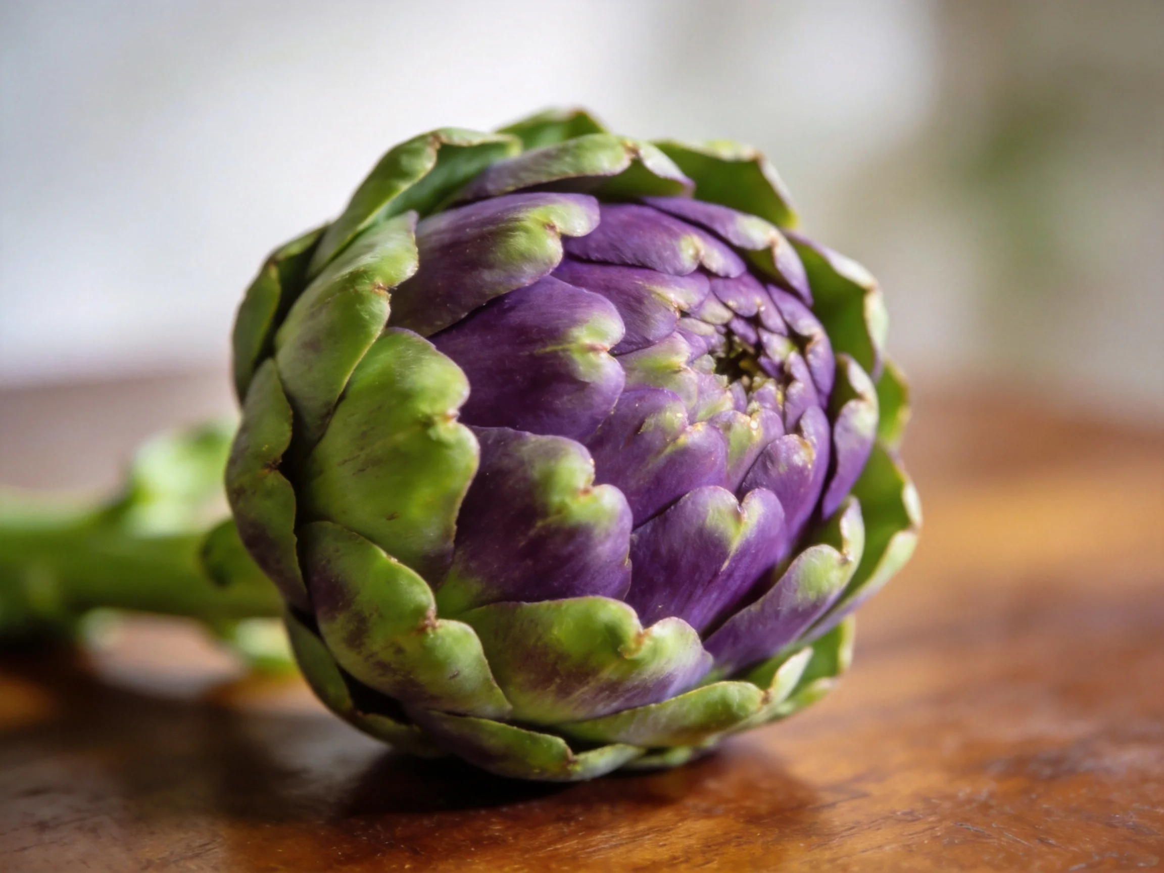 A vibrant purple and green artichoke resting on a wooden surface