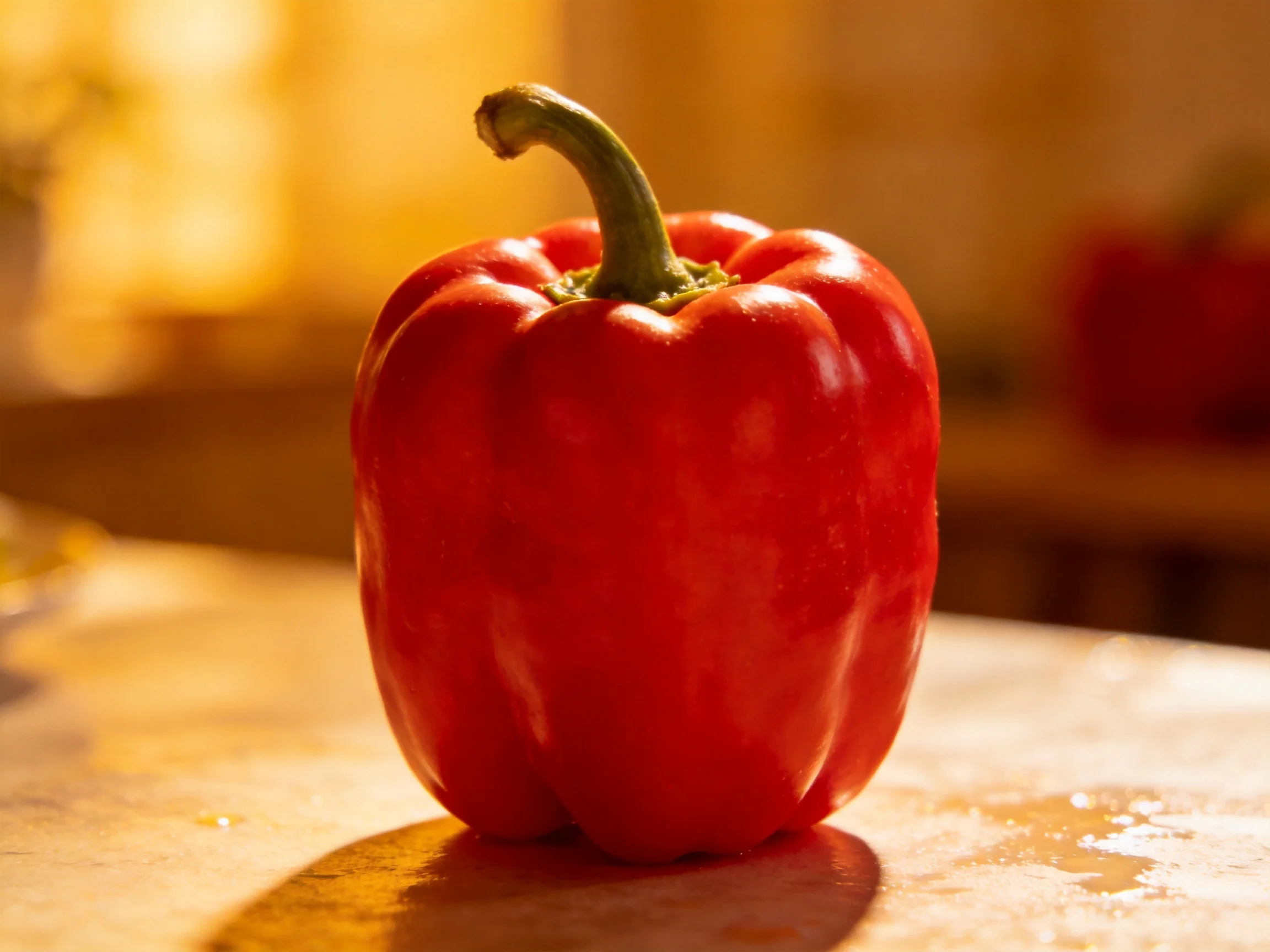 A vibrant red bell pepper sits on a wooden surface with warm lighting.