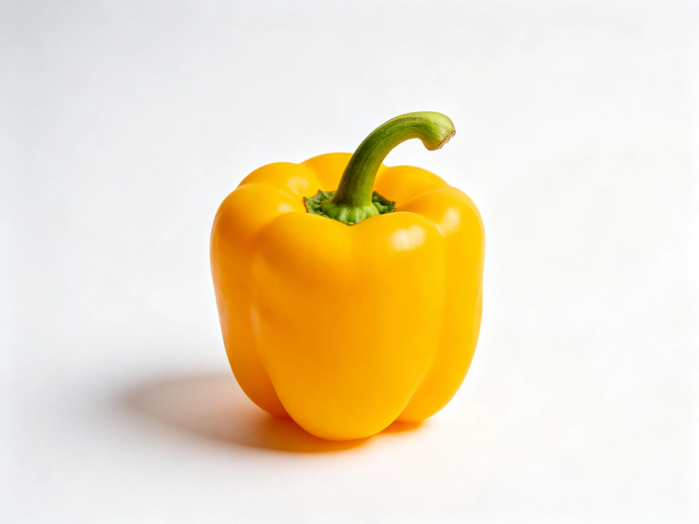 A vibrant yellow bell pepper with a curved green stem on a white surface