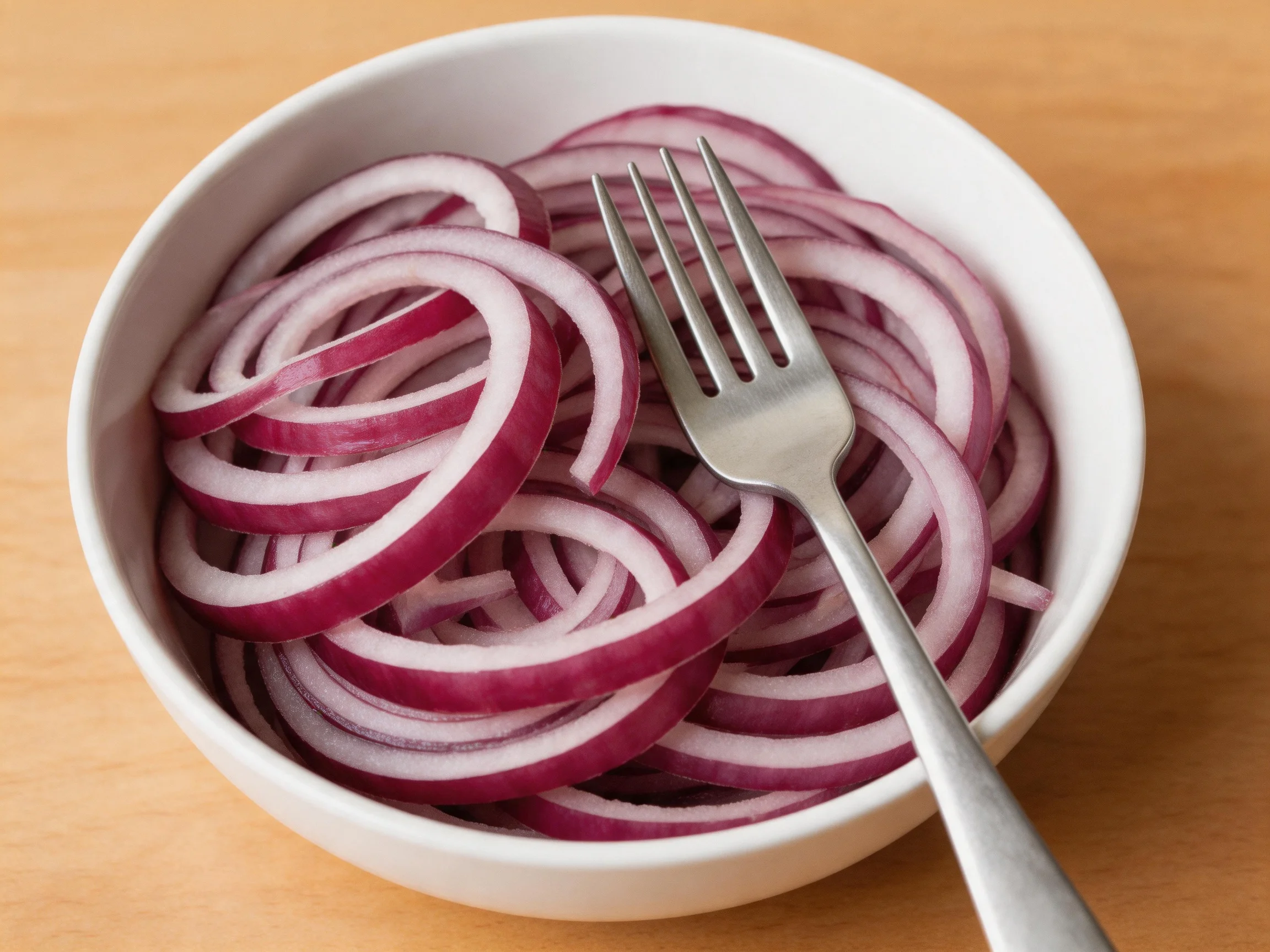 A white bowl filled with thickly sliced red-purple onion rings and a silver fork