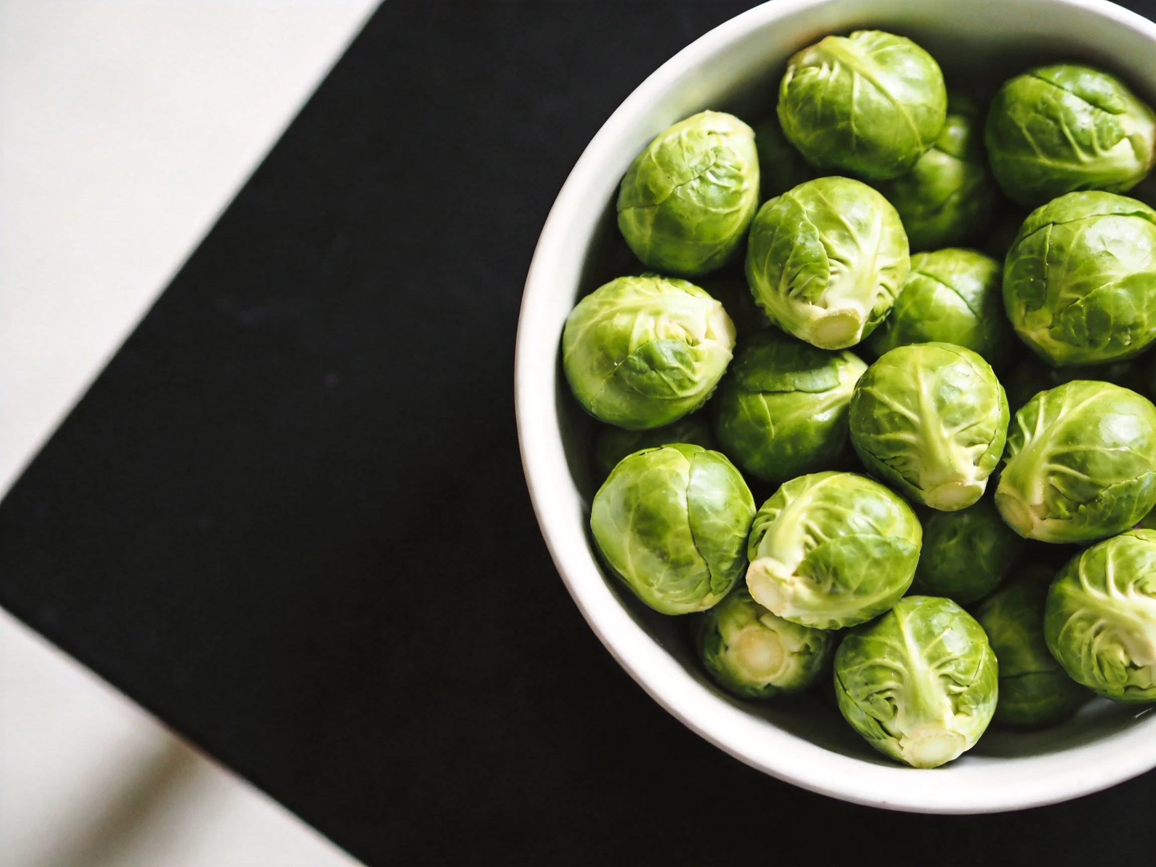A white bowl holding numerous fresh green Brussels sprouts