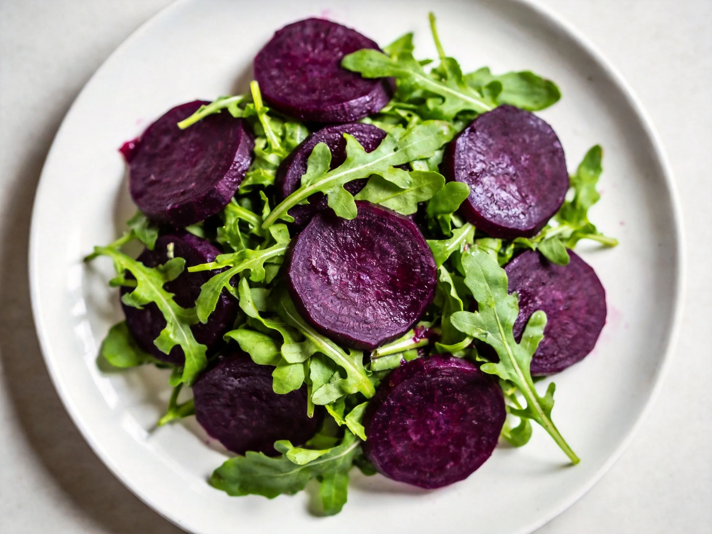 A white plate displays sliced purple beets and fresh arugula greens