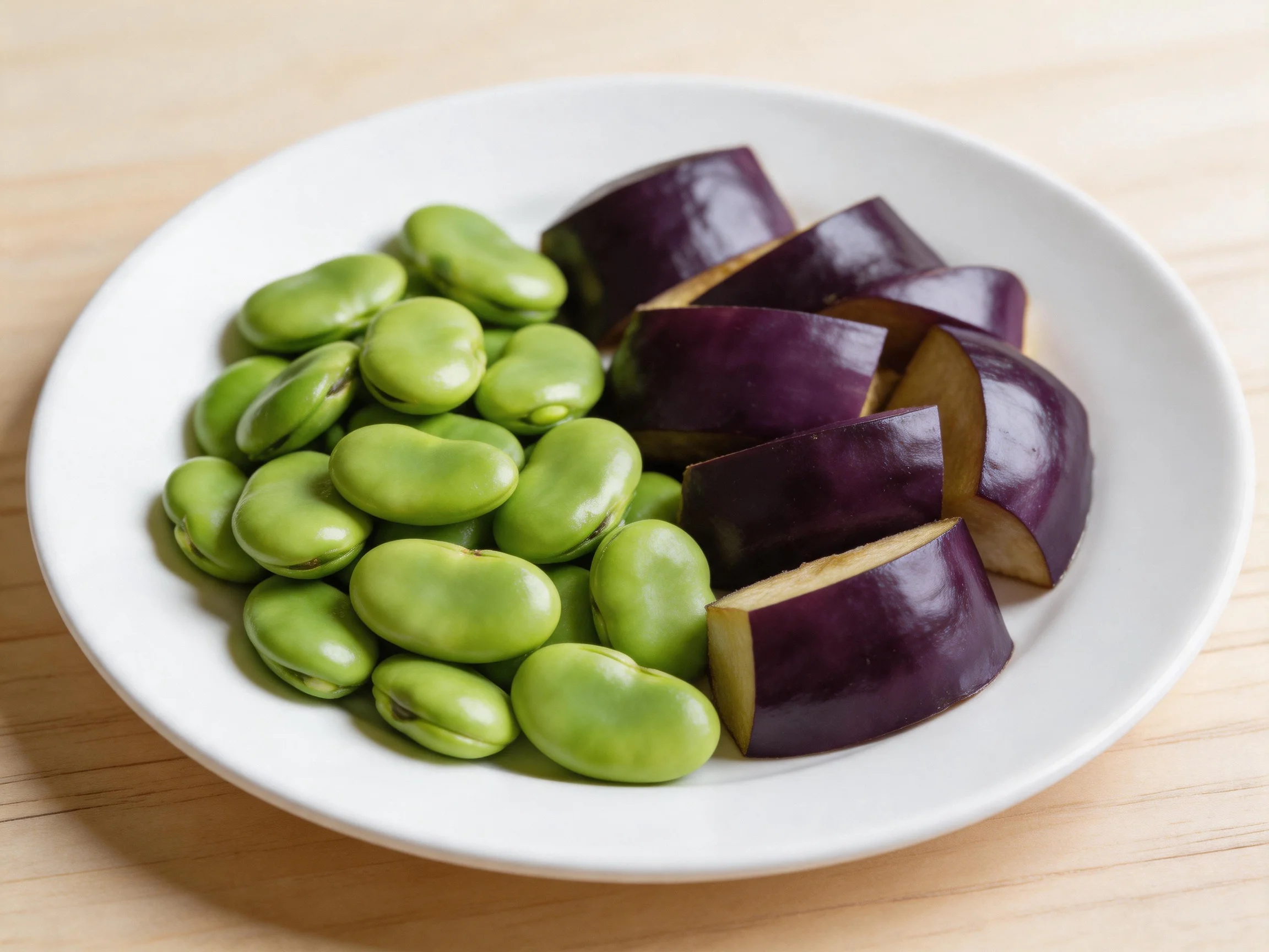 A white plate holds green broad beans and purple eggplant slices