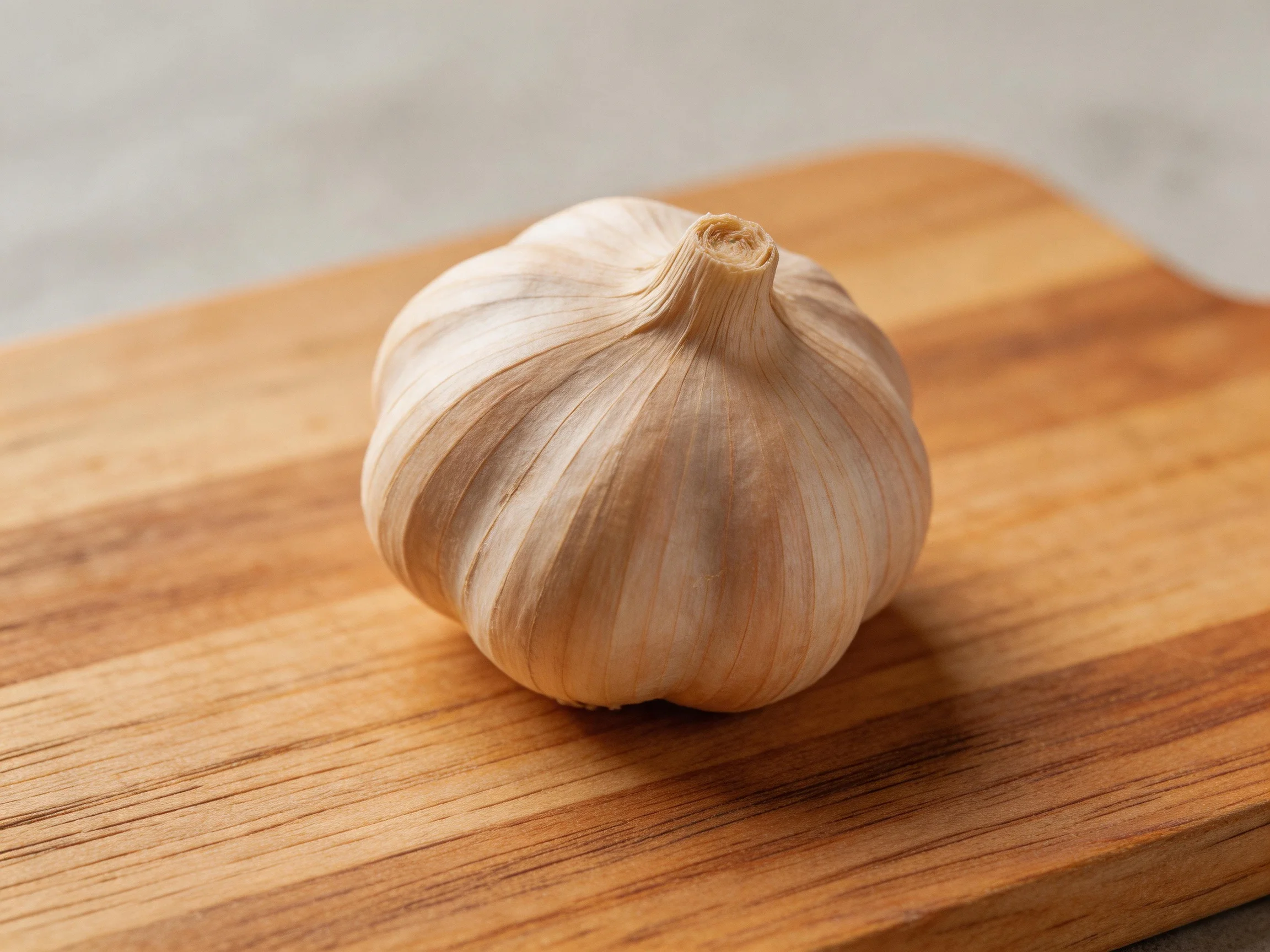 A whole garlic bulb resting on a polished wooden cutting board