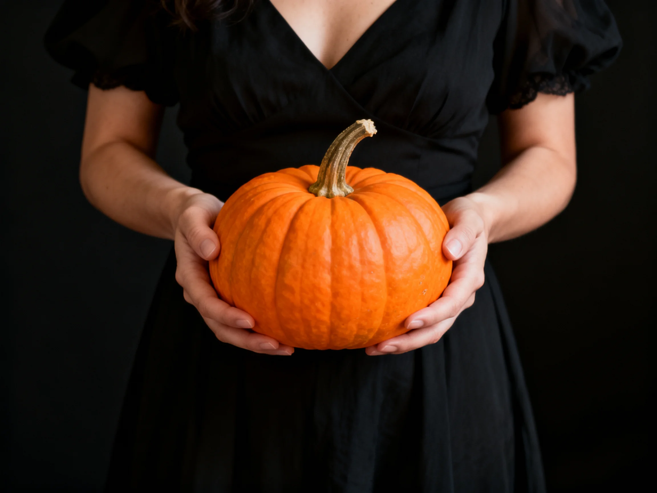 A woman in a black dress holds a large orange pumpkin
