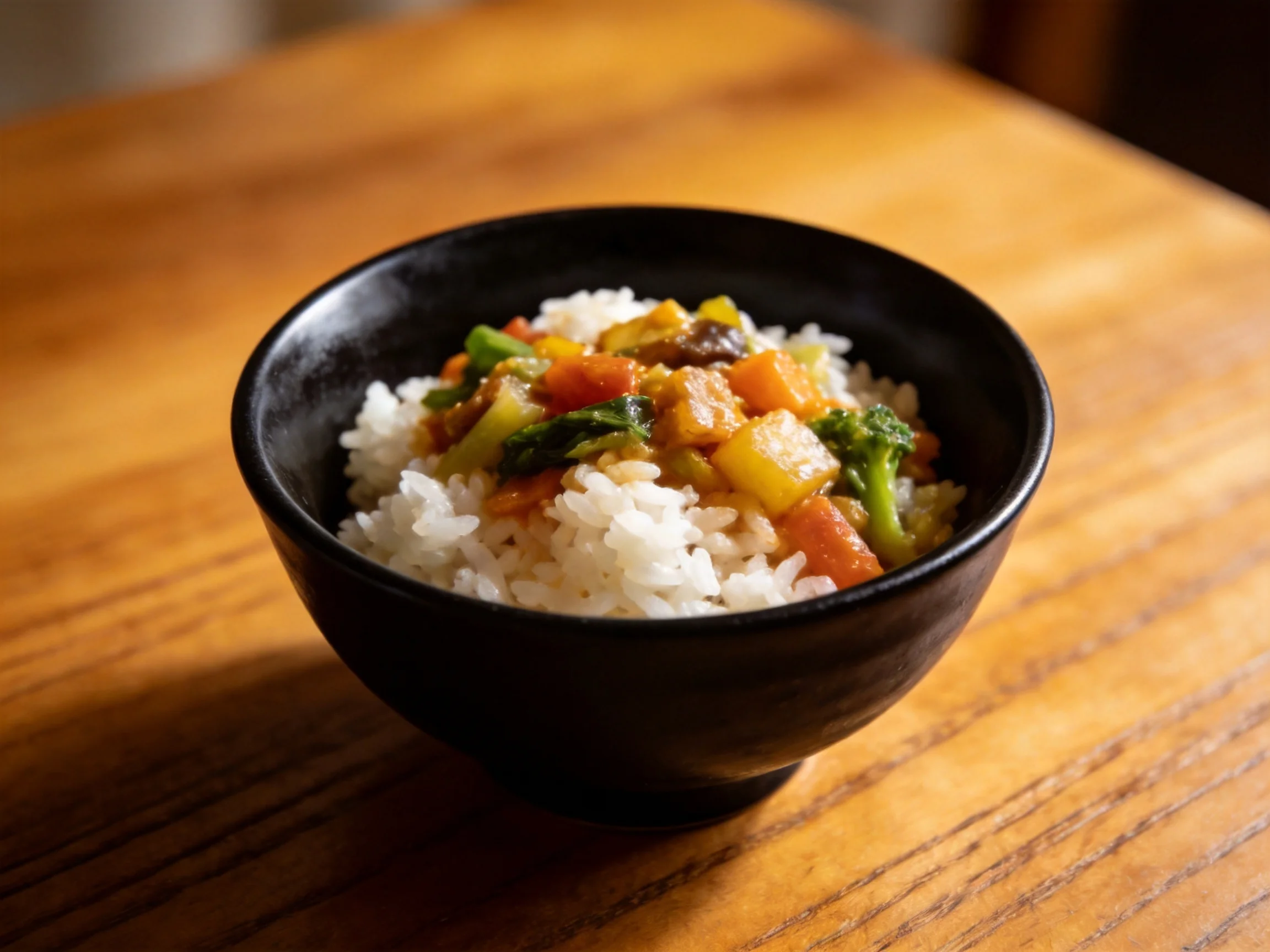 Black bowl holding fluffy white rice with assorted vegetable medley