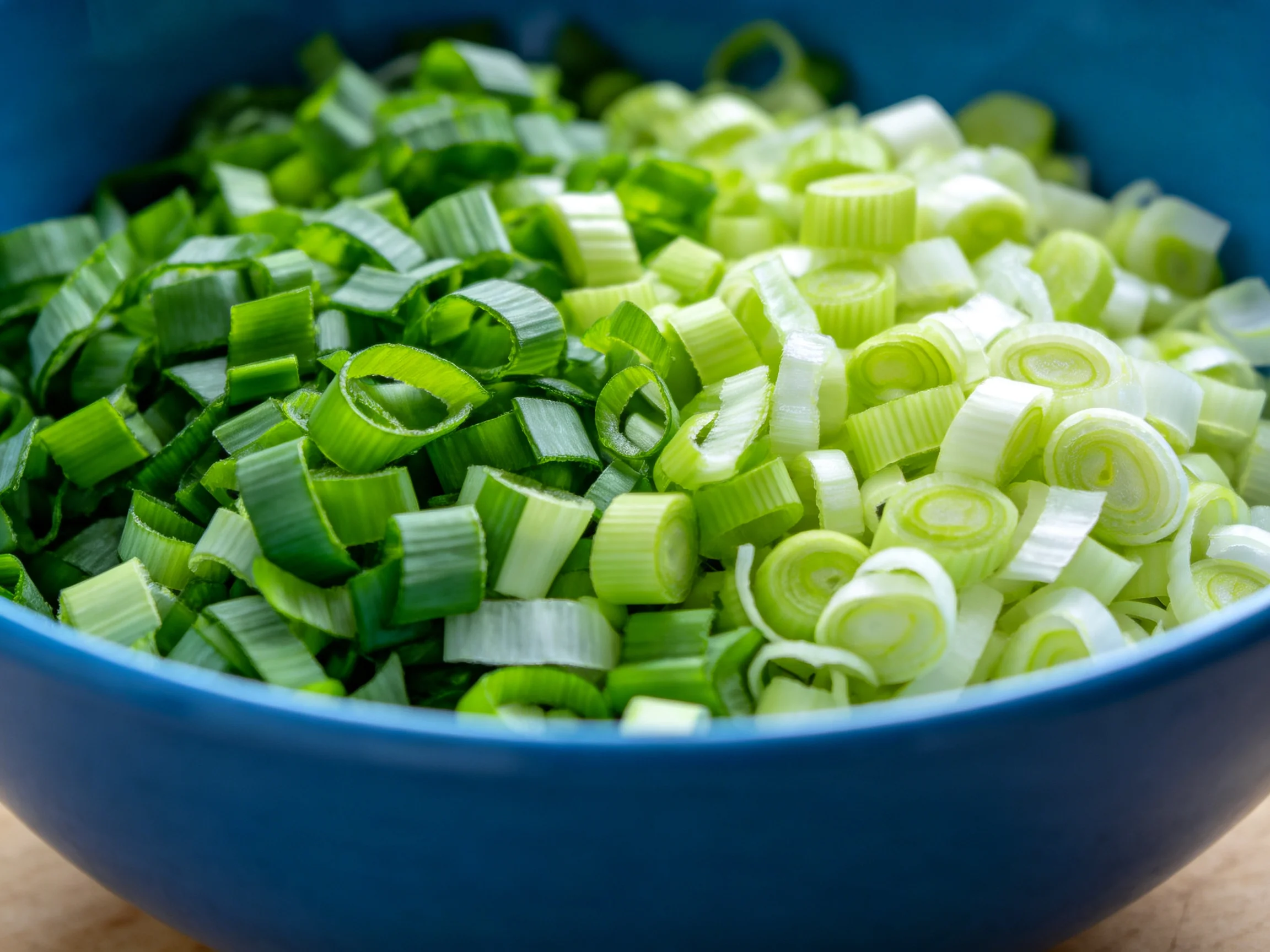 Chopped green onions in a blue bowl with two shades of green