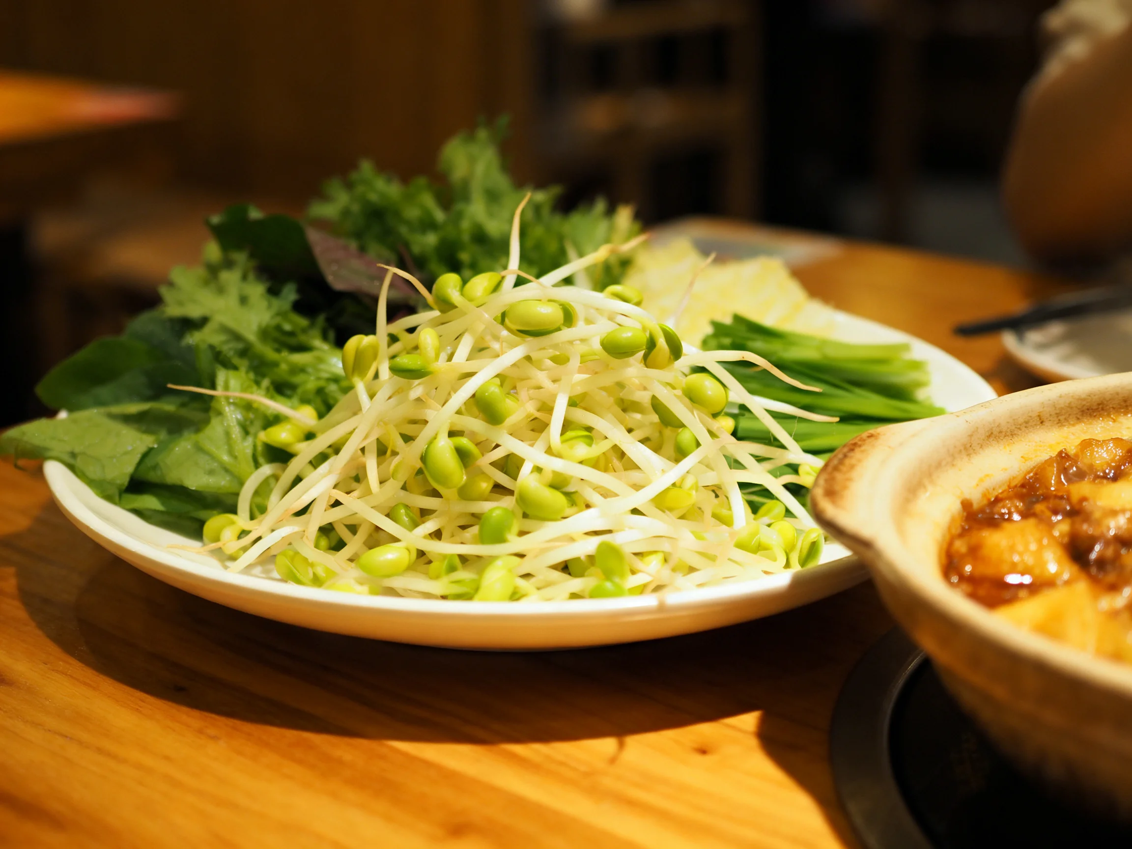 Edamame sprout and mixed green vegetable platter beside a savory bowl