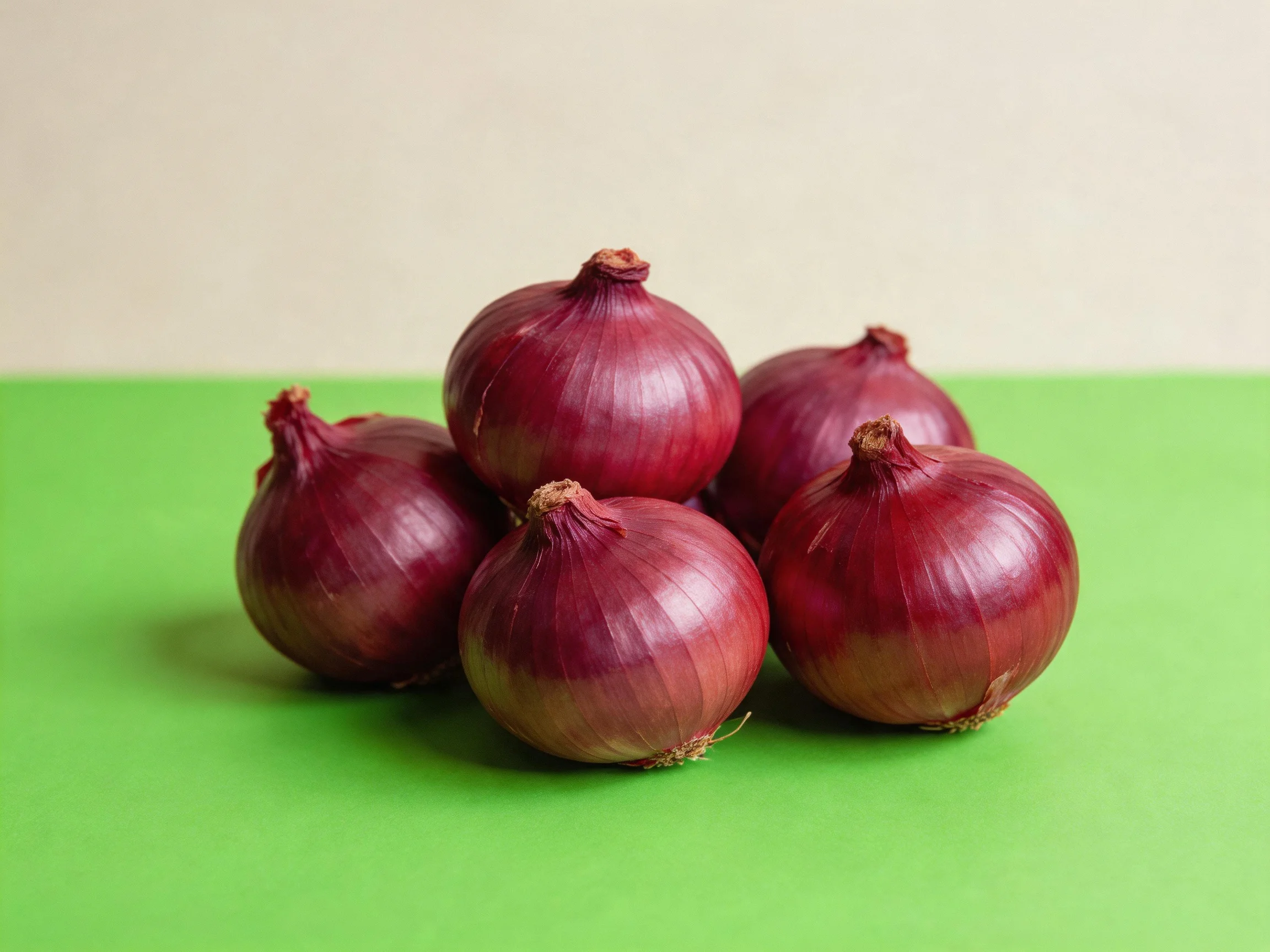 Five deep red onions clustered on a bright green surface