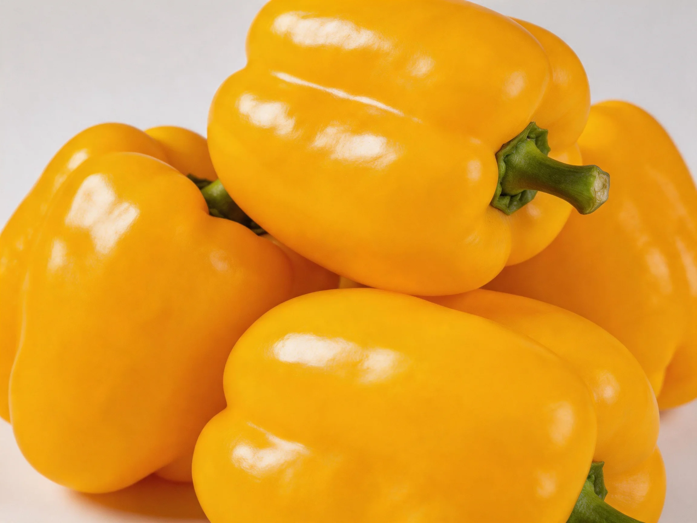 Five vibrant yellow bell peppers stacked with green stems