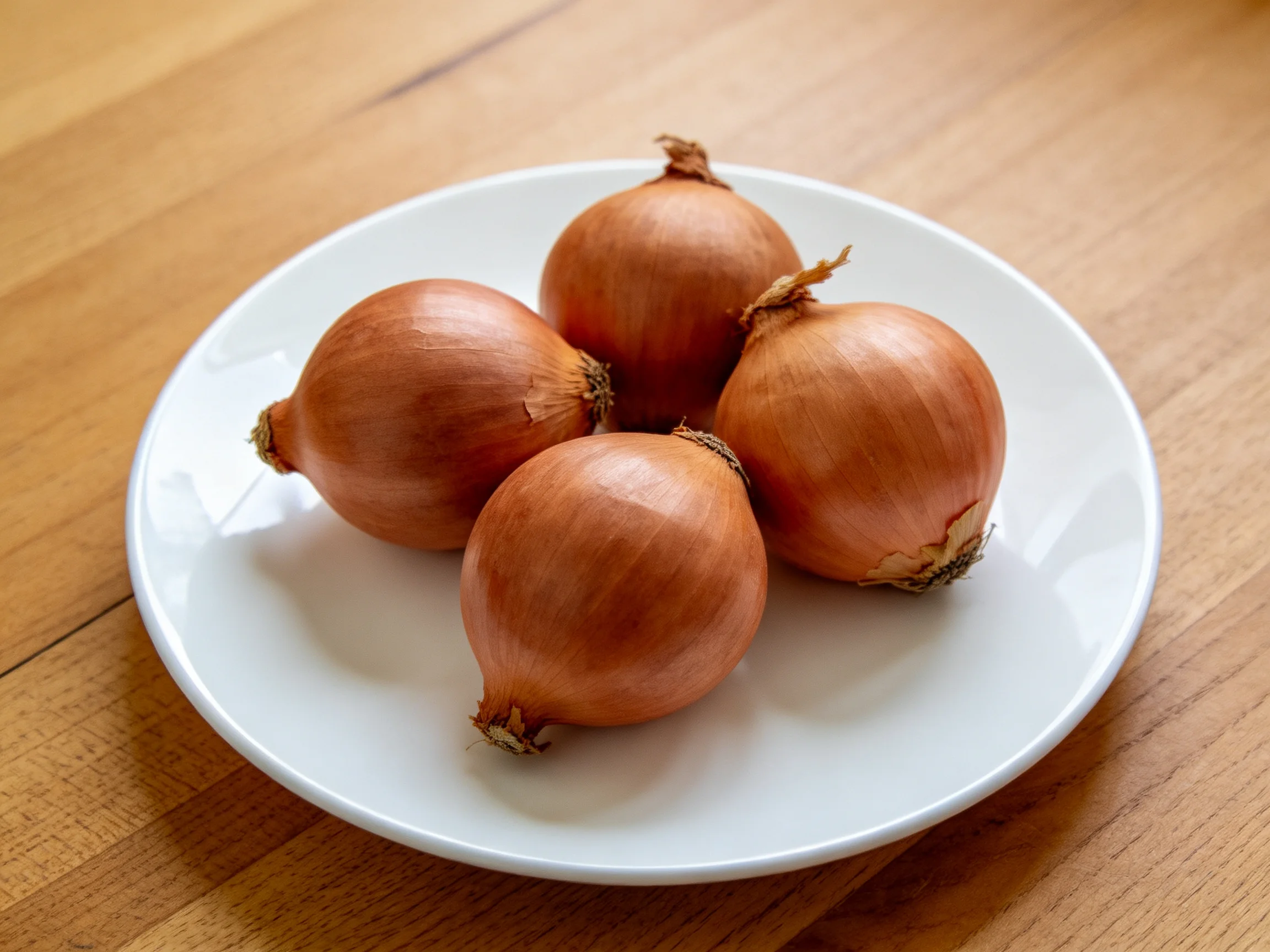 Four golden-brown onions arranged on a white plate on a wooden surface