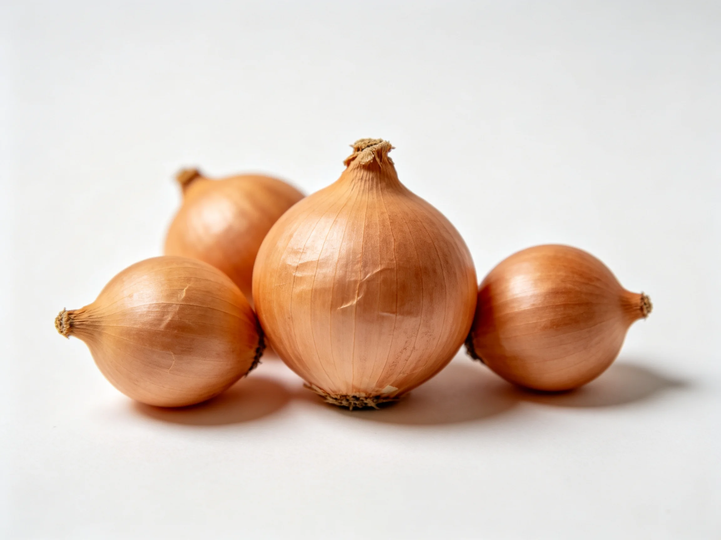 Four golden-brown onions clustered on a plain white surface