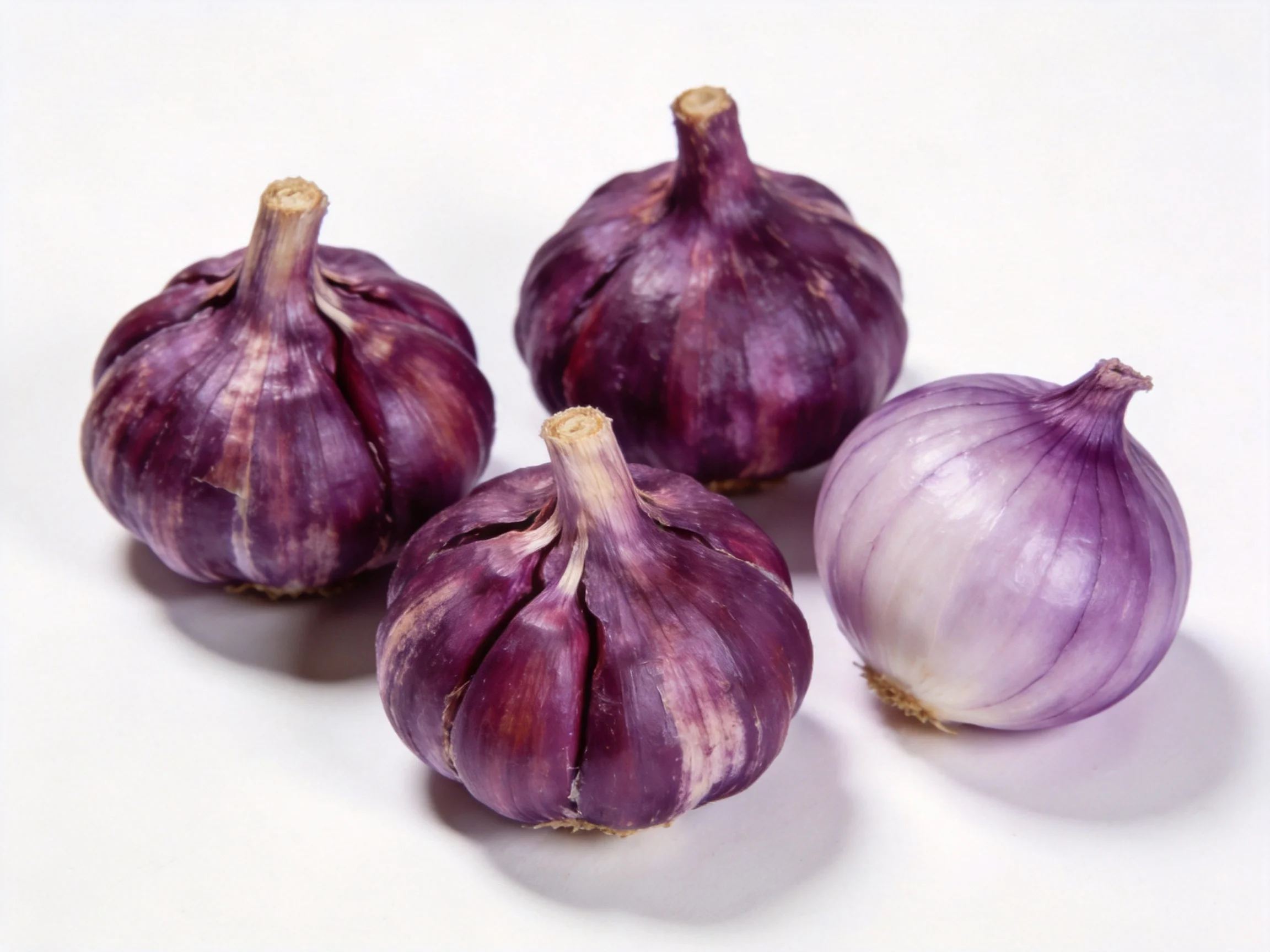 Four purple garlic bulbs and one light purple onion on a white surface