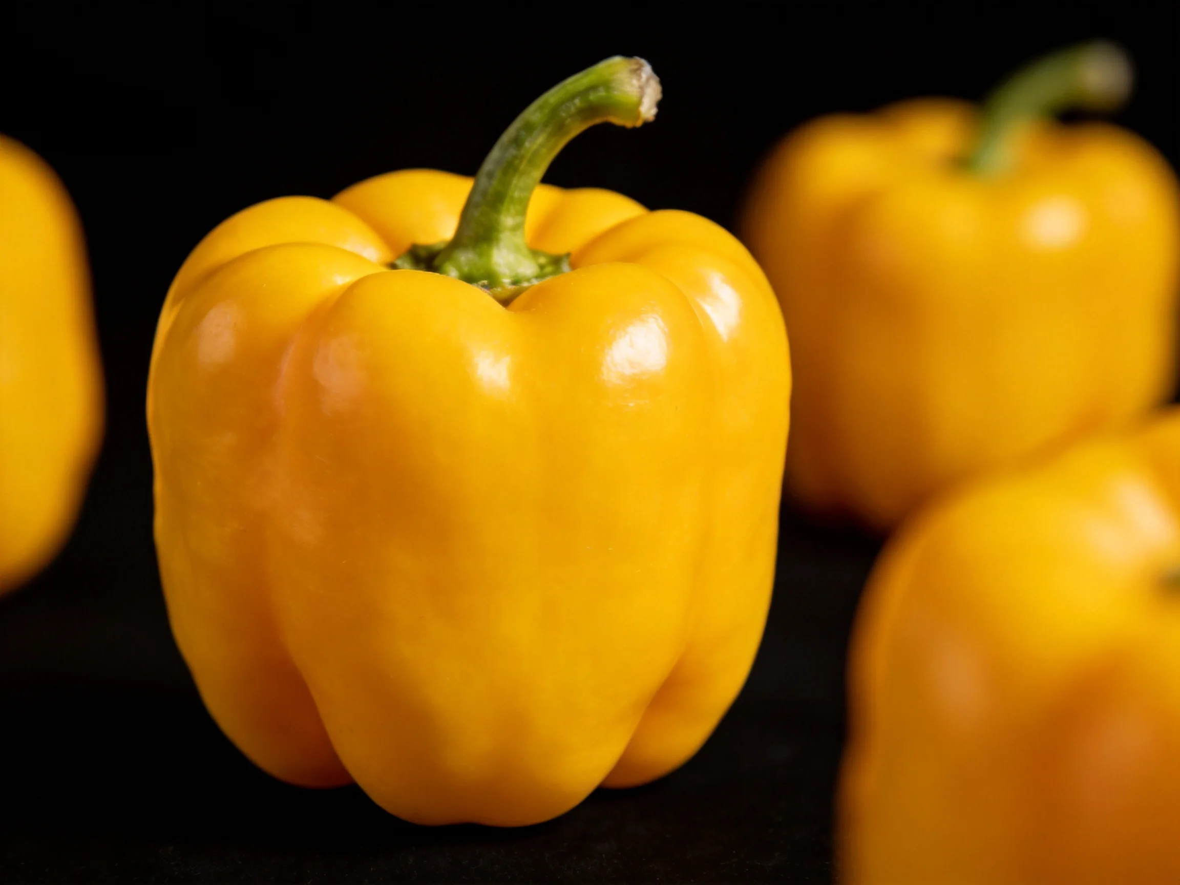 Four vibrant yellow bell peppers displayed on a dark surface