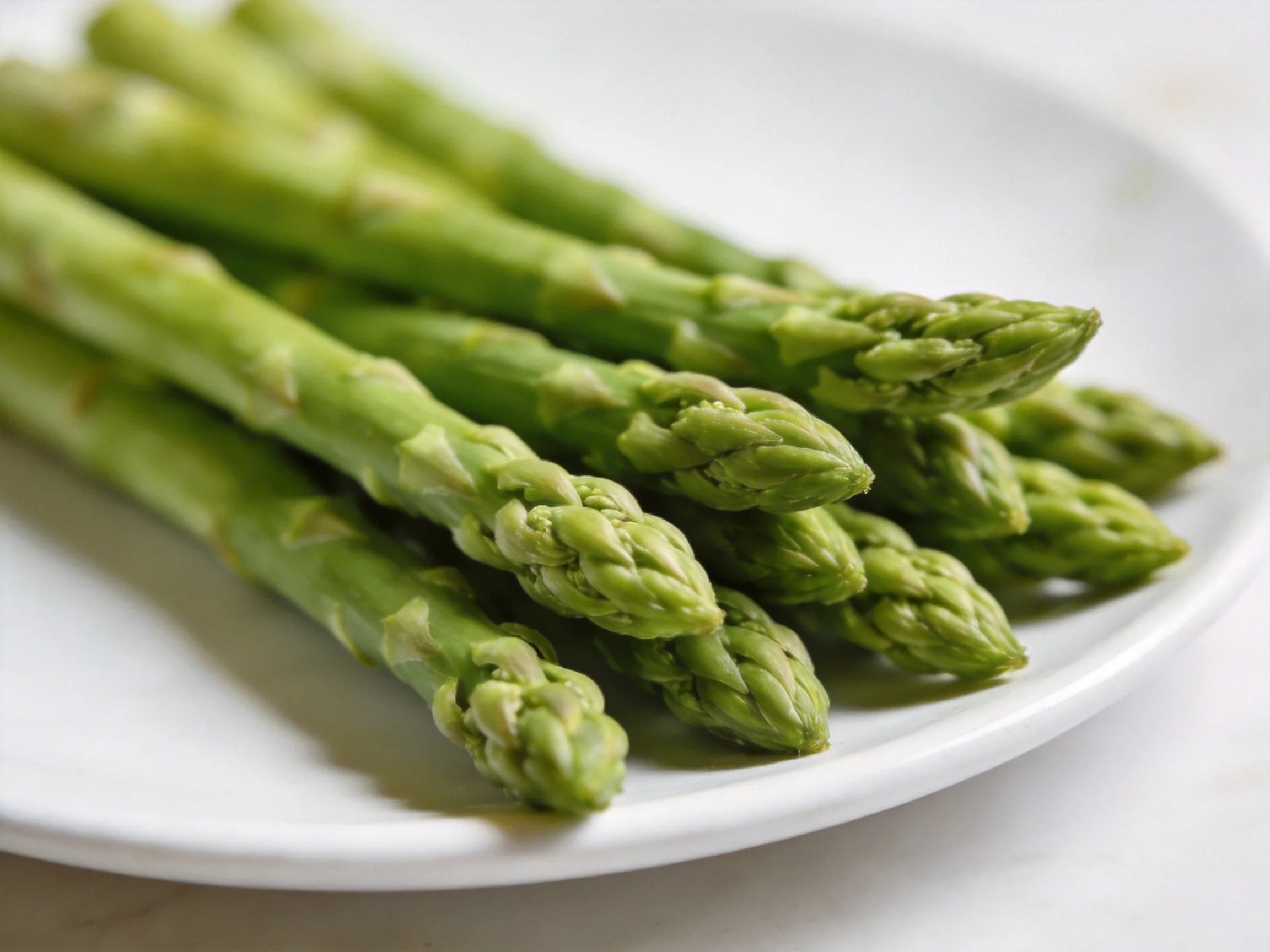 Fresh green asparagus spears arranged on a plain white plate