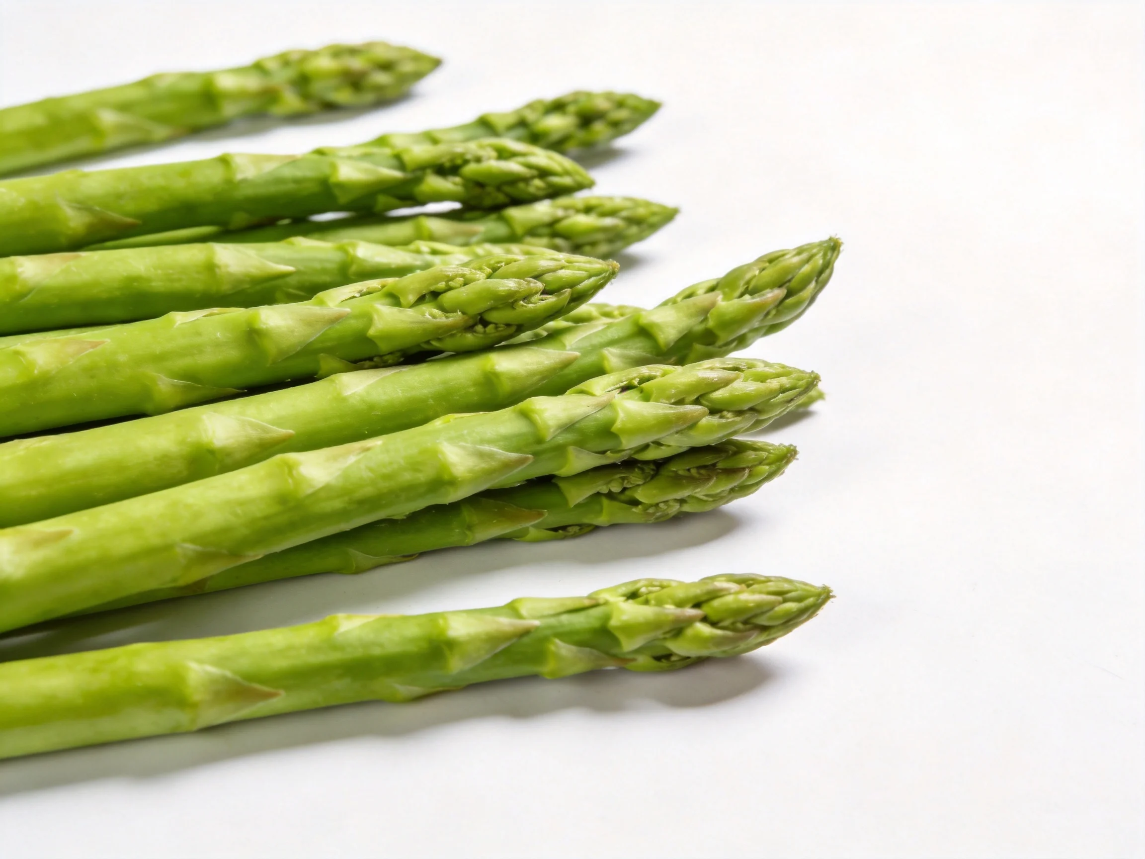 Fresh green asparagus spears clustered diagonally on white surface