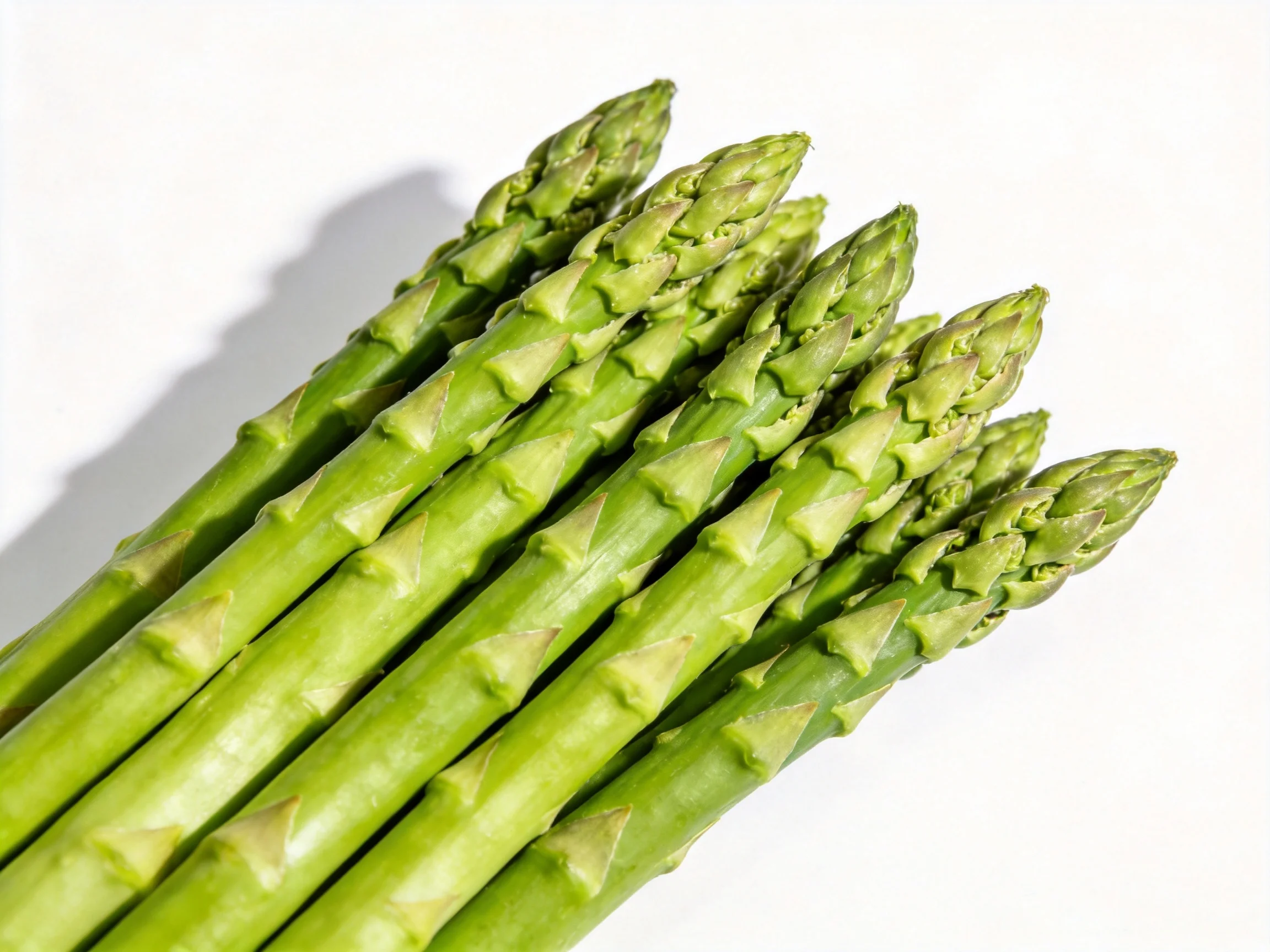 Fresh green asparagus spears clustered tightly on a white surface