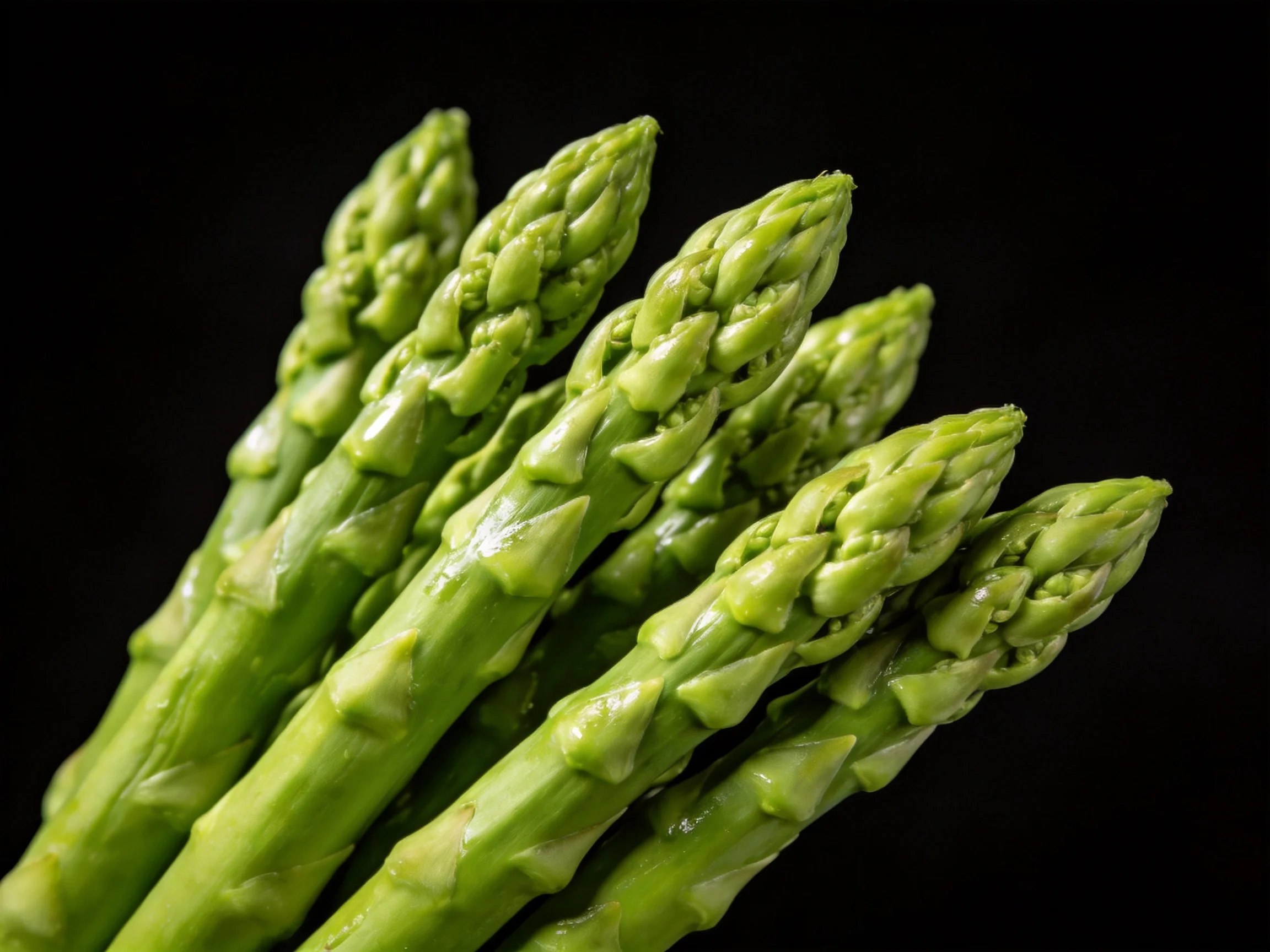 Fresh green asparagus spears with textured tips against a solid black background