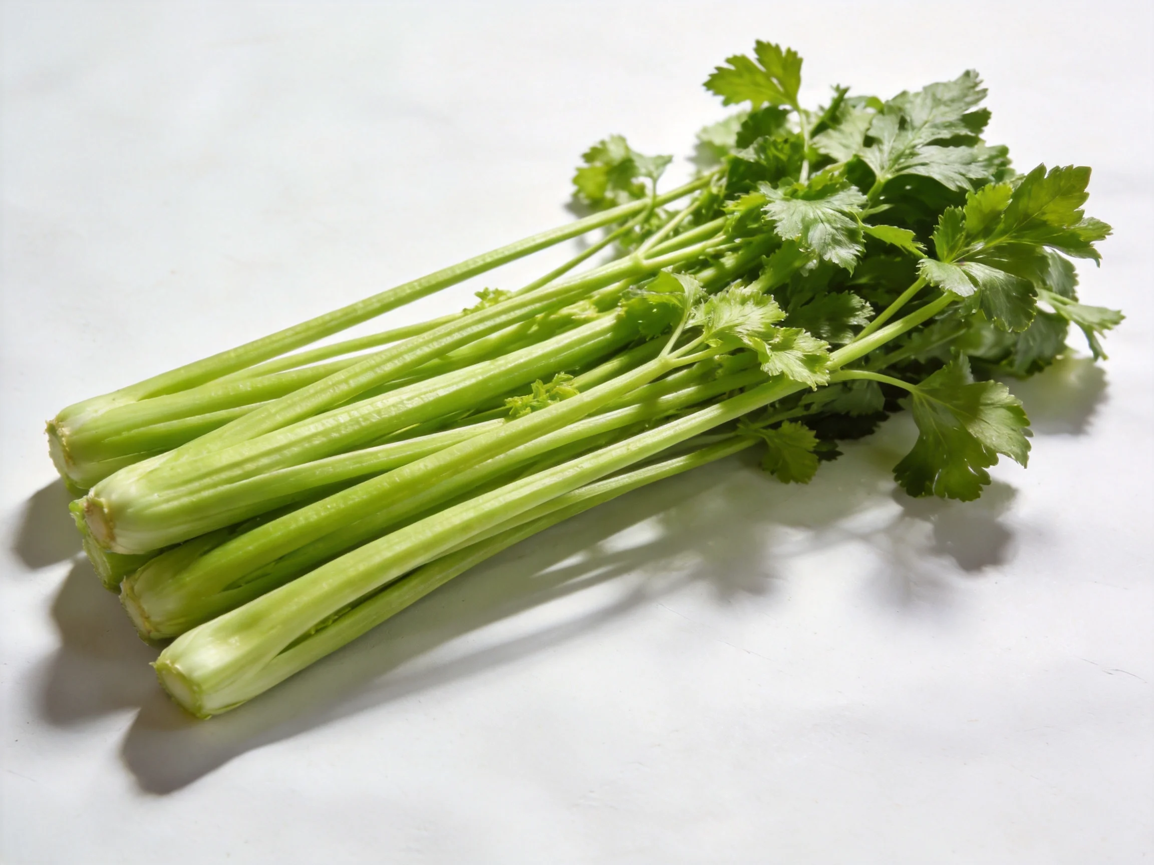 Fresh green celery stalks with leafy tops on a white surface