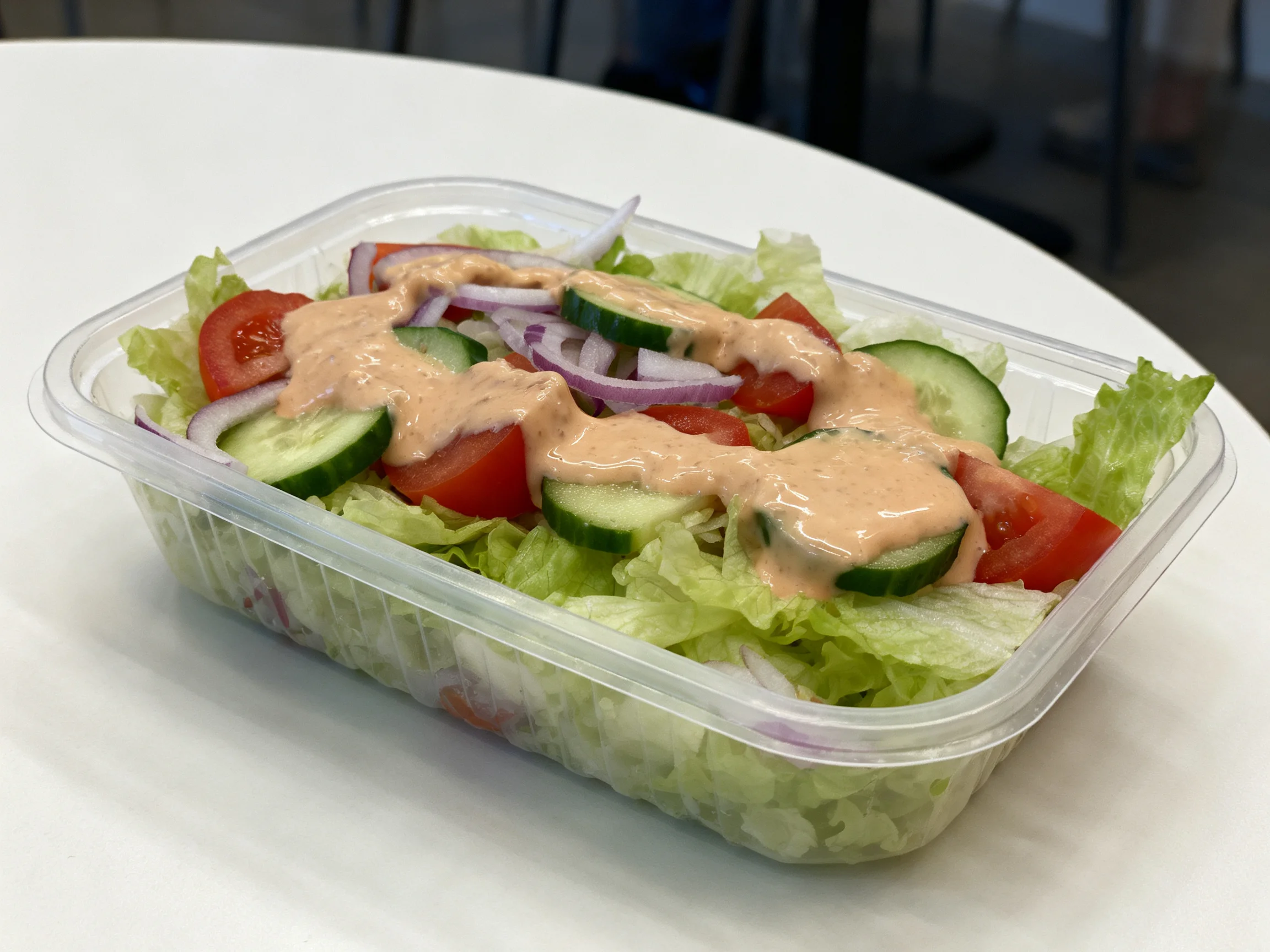 Fresh vegetable salad with tomatoes, cucumbers, onions, and creamy dressing in plastic container