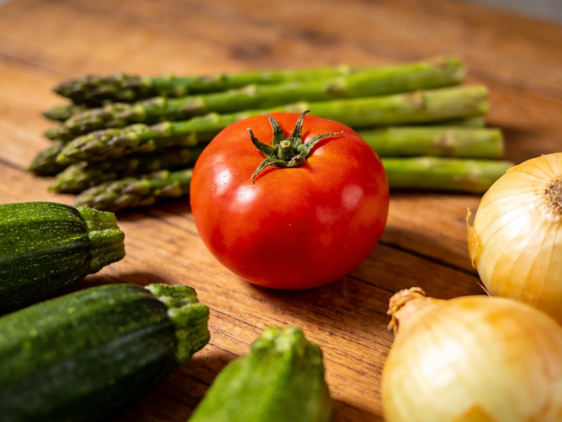 Fresh vegetables—including tomato, asparagus, zucchini, and onions—arranged on a wooden surface