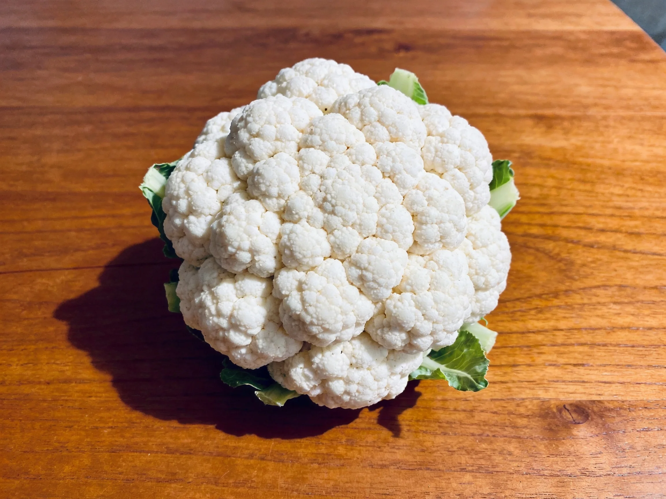 Fresh white cauliflower with green leaves on a polished wooden table