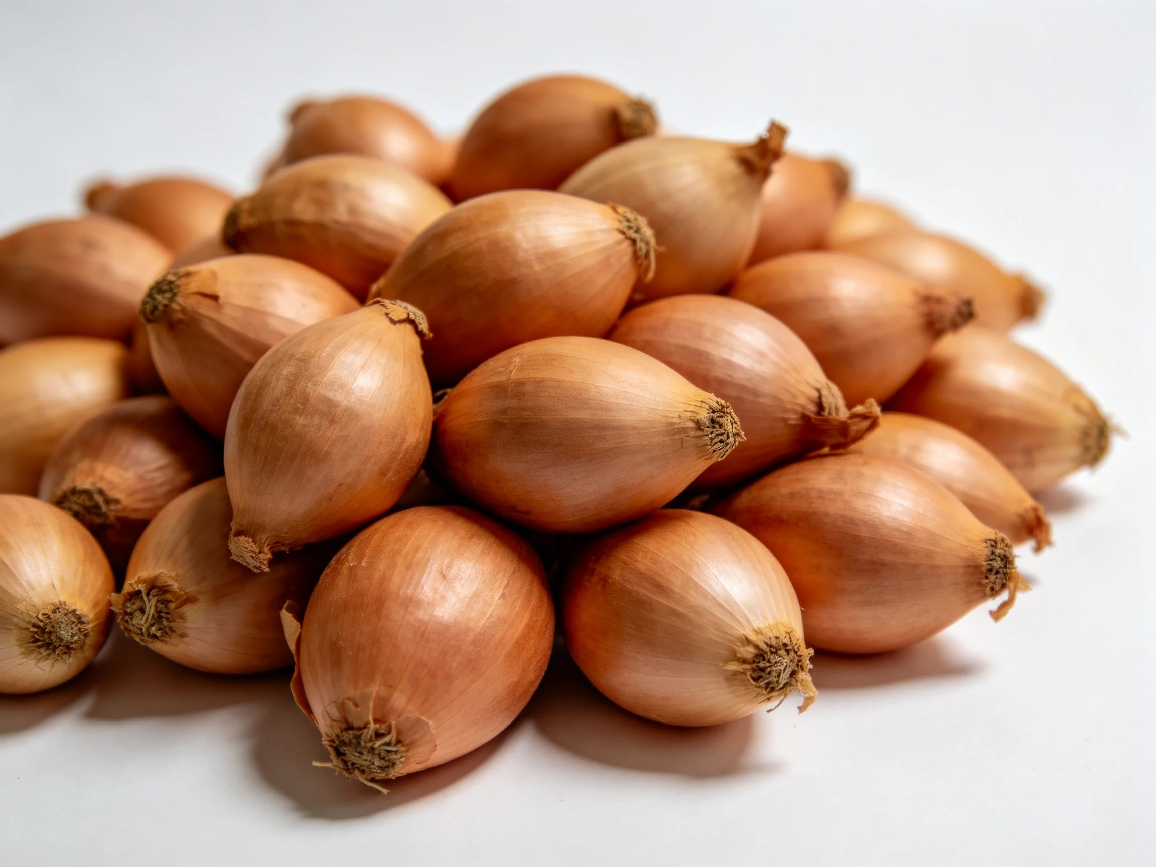 Golden-brown shallots clustered in a dense pile on a white surface