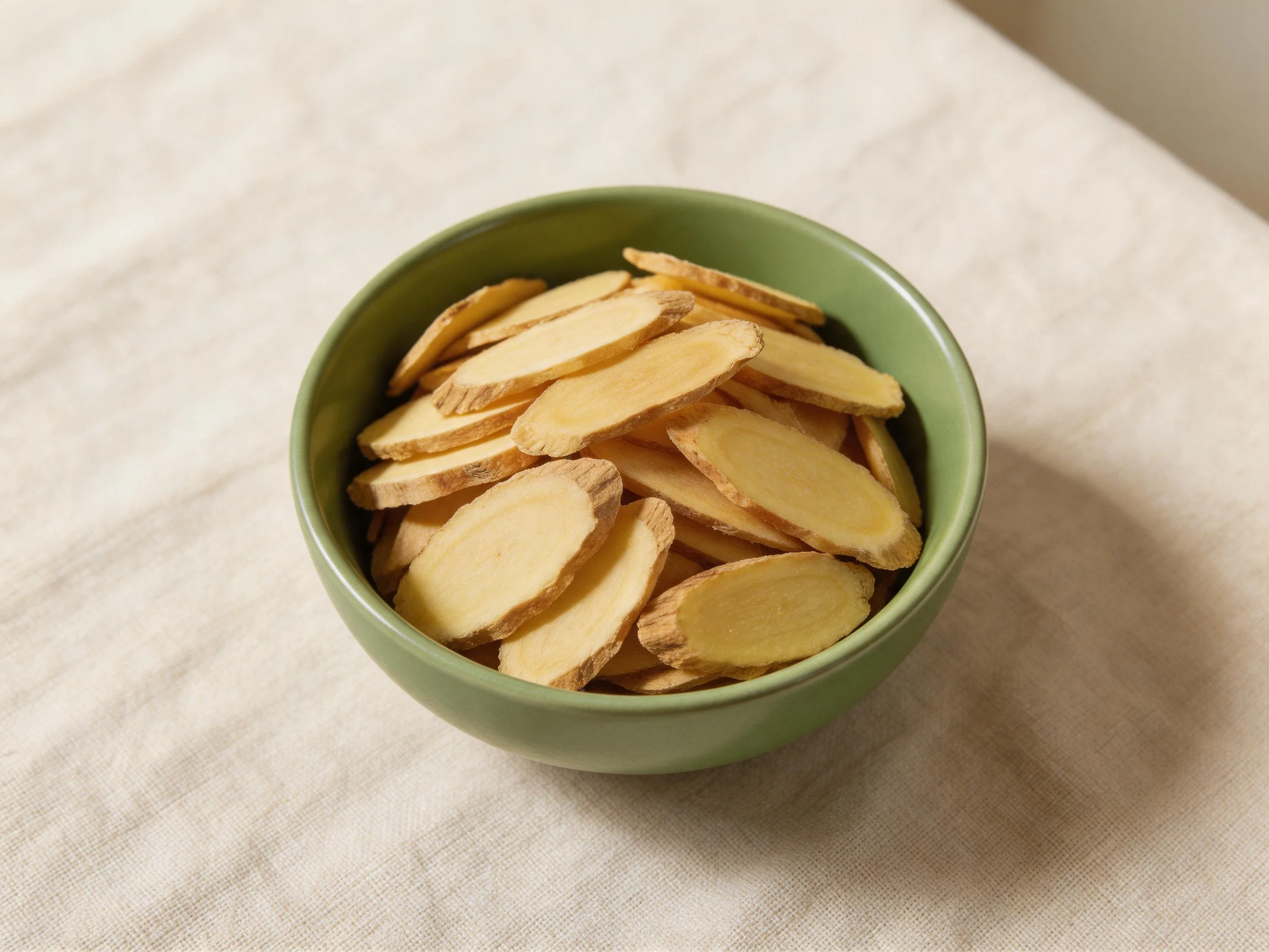 Green bowl with sliced dried ginger on white fabric