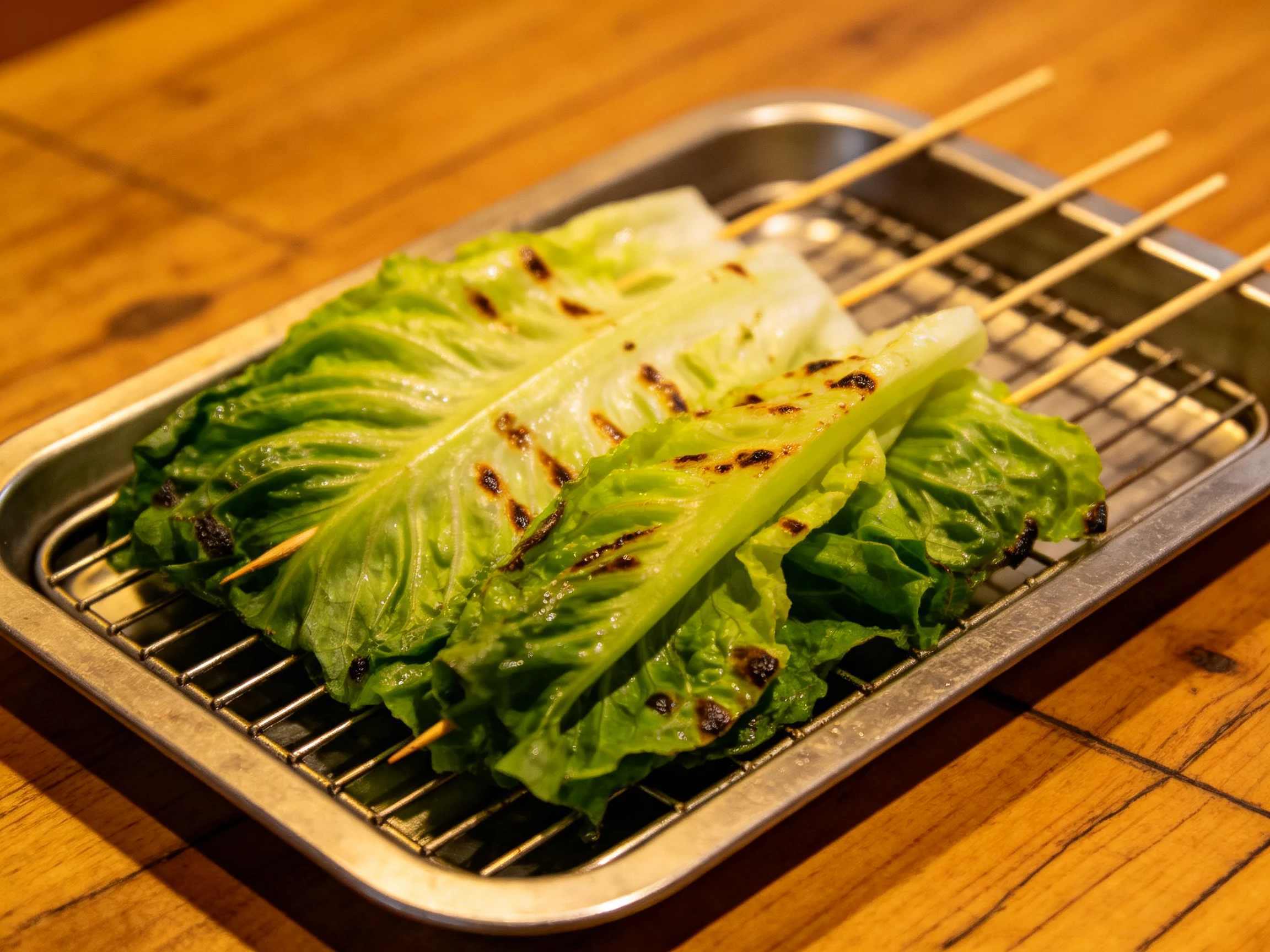 Grilled romaine lettuce leaves on wooden skewers in metal tray