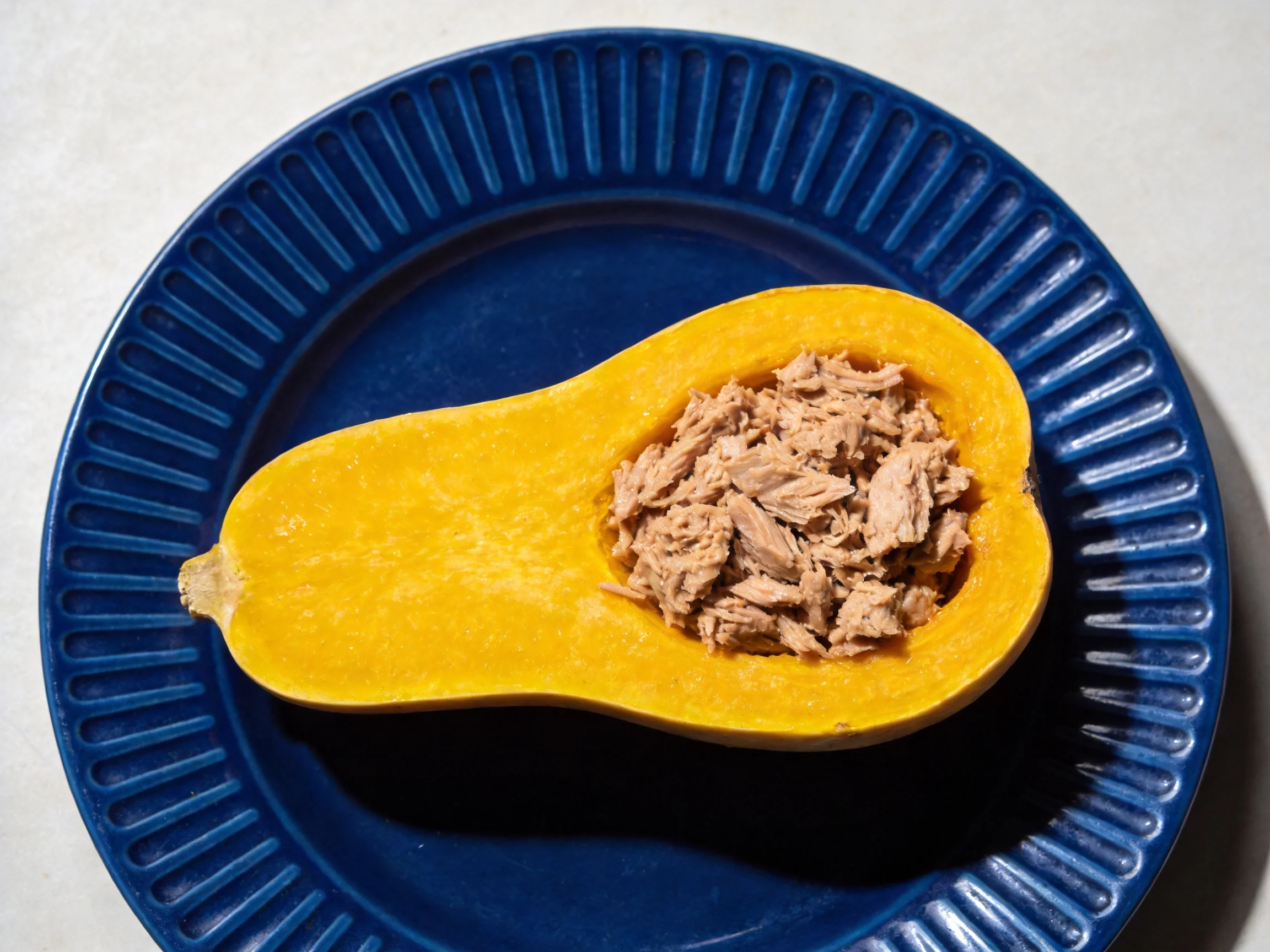 Halved yellow squash stuffed with tuna on a deep blue plate