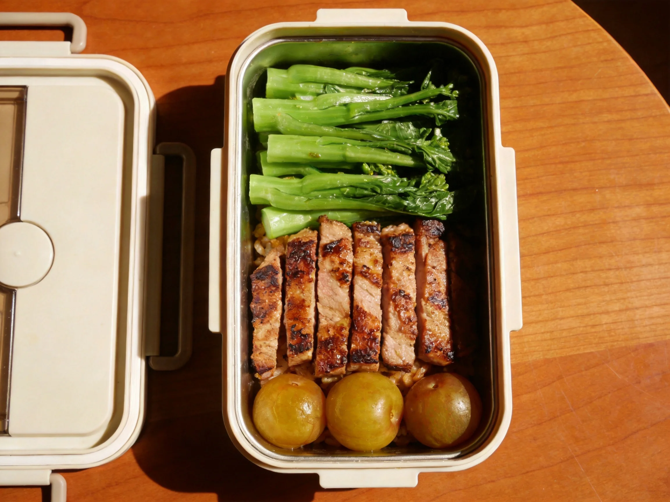 Neatly arranged bento box with green vegetables, grilled meat, and round fruits