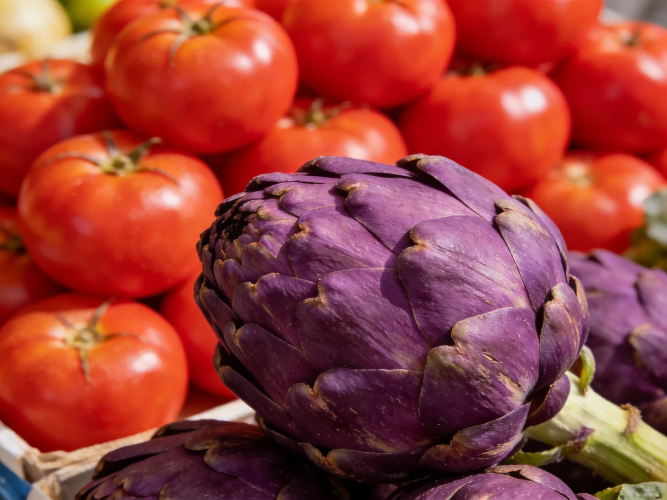 Purple artichokes and red tomatoes displayed at a market