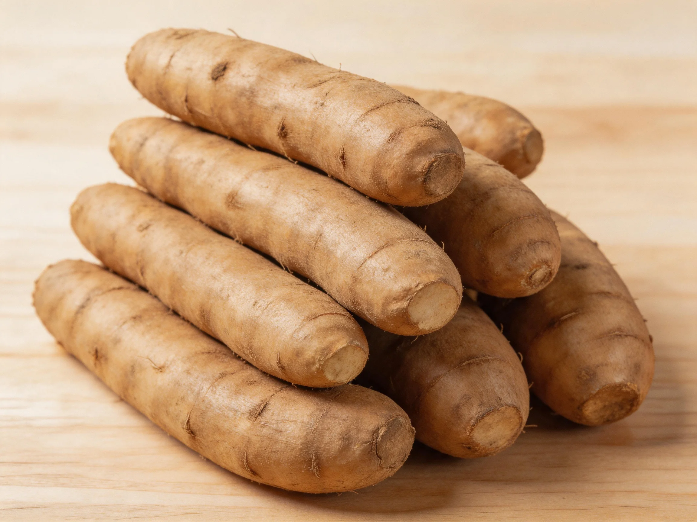 Several beige tubers stacked in a pyramid on a light wooden surface