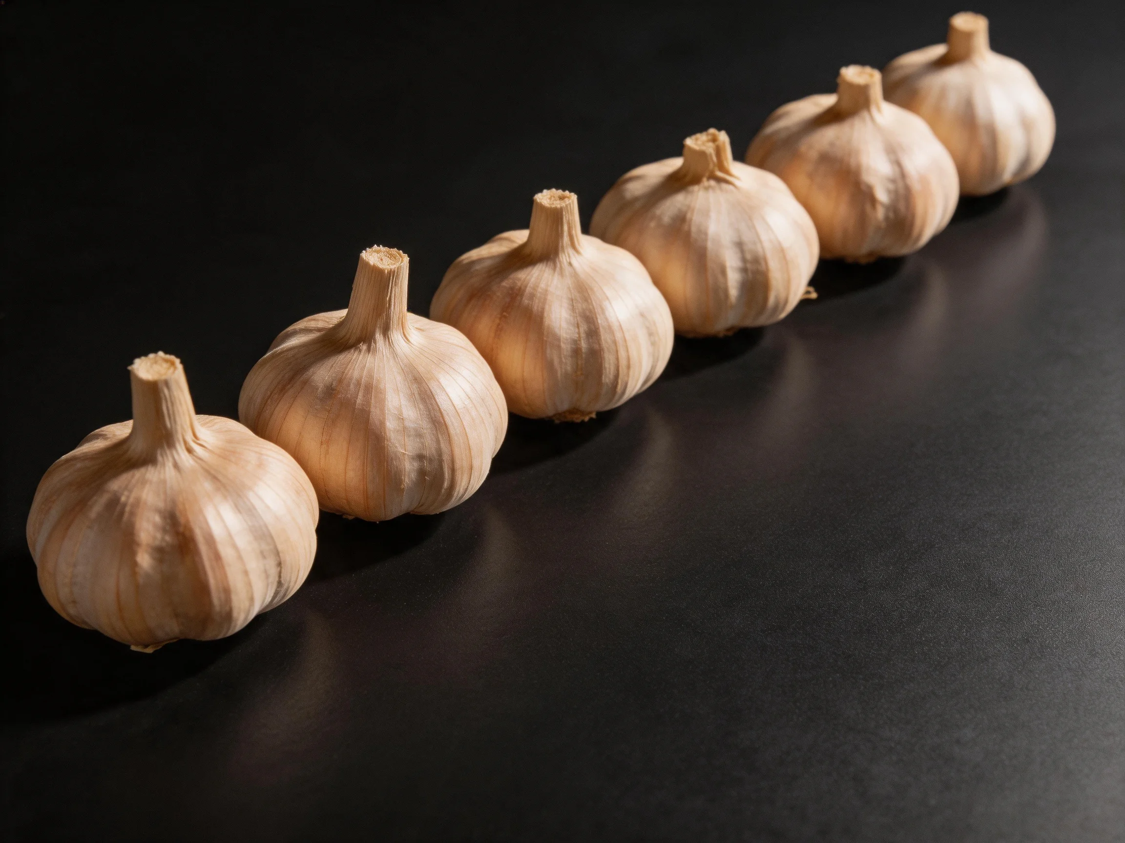 Six garlic bulbs are neatly lined up on a dark surface