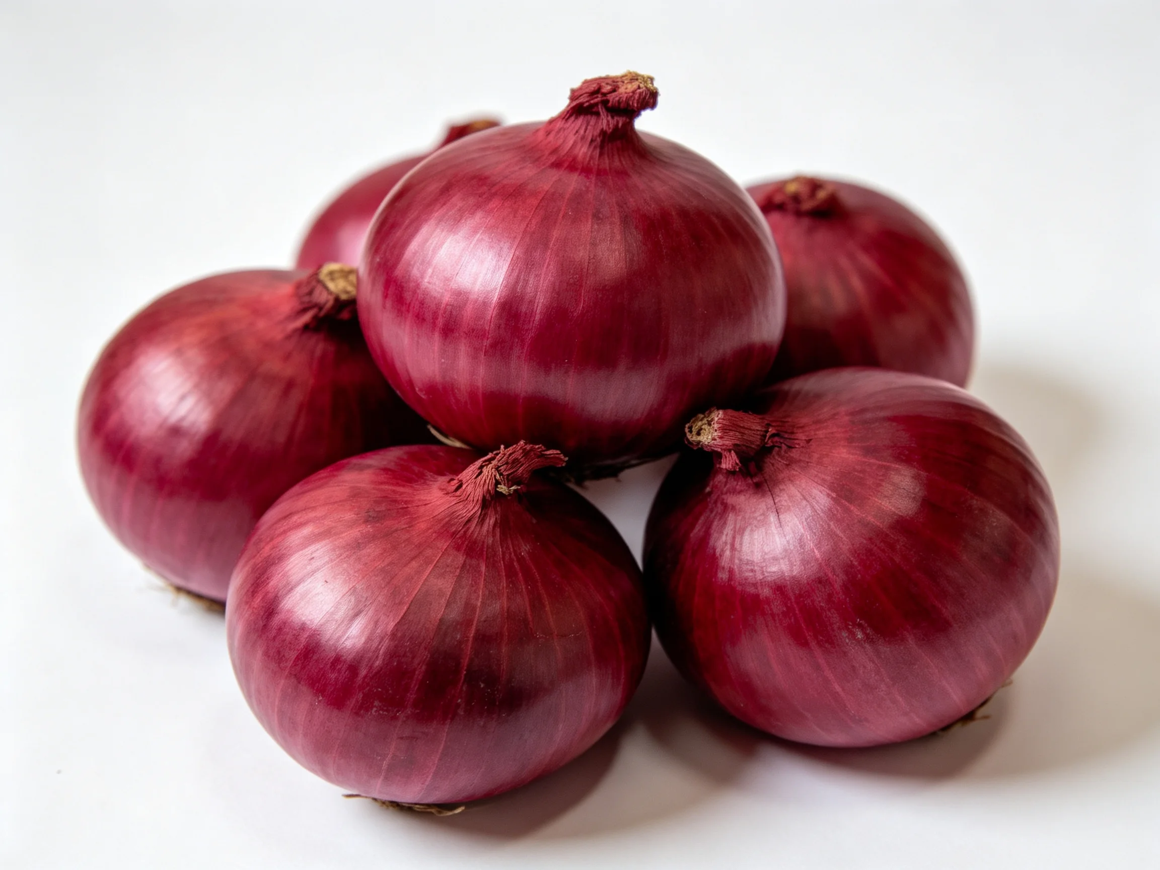 Six glossy red onions clustered on a plain white surface
