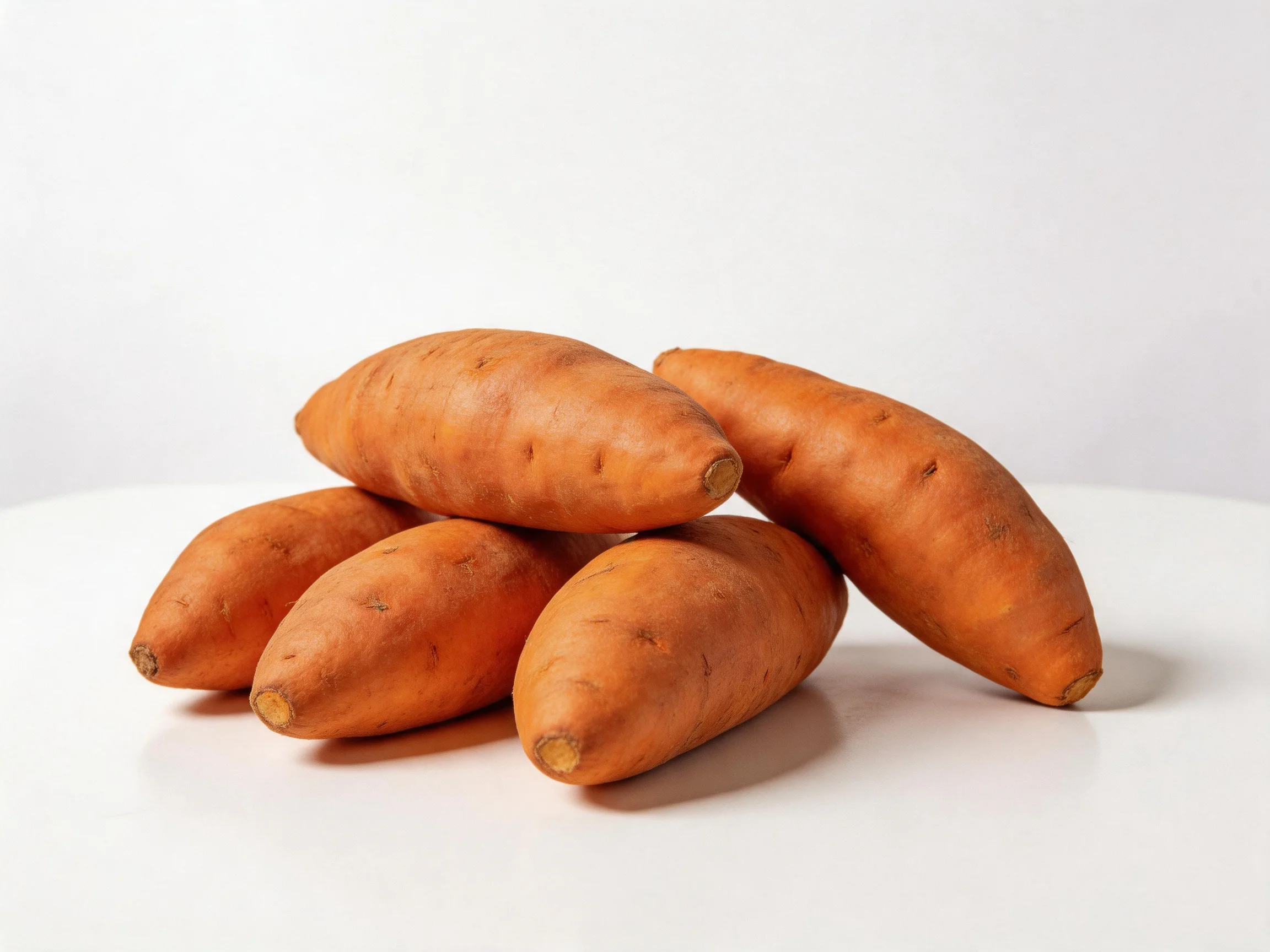 Six orange sweet potato tubers stacked on a plain white surface