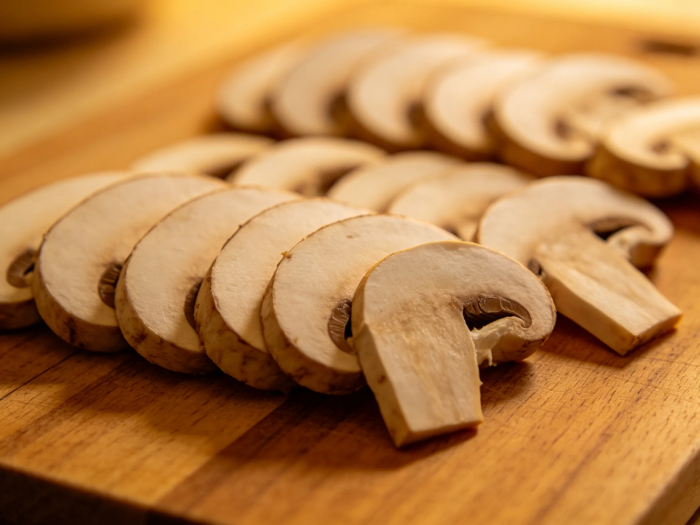 Sliced mushrooms arranged in neat rows on a wooden cutting board