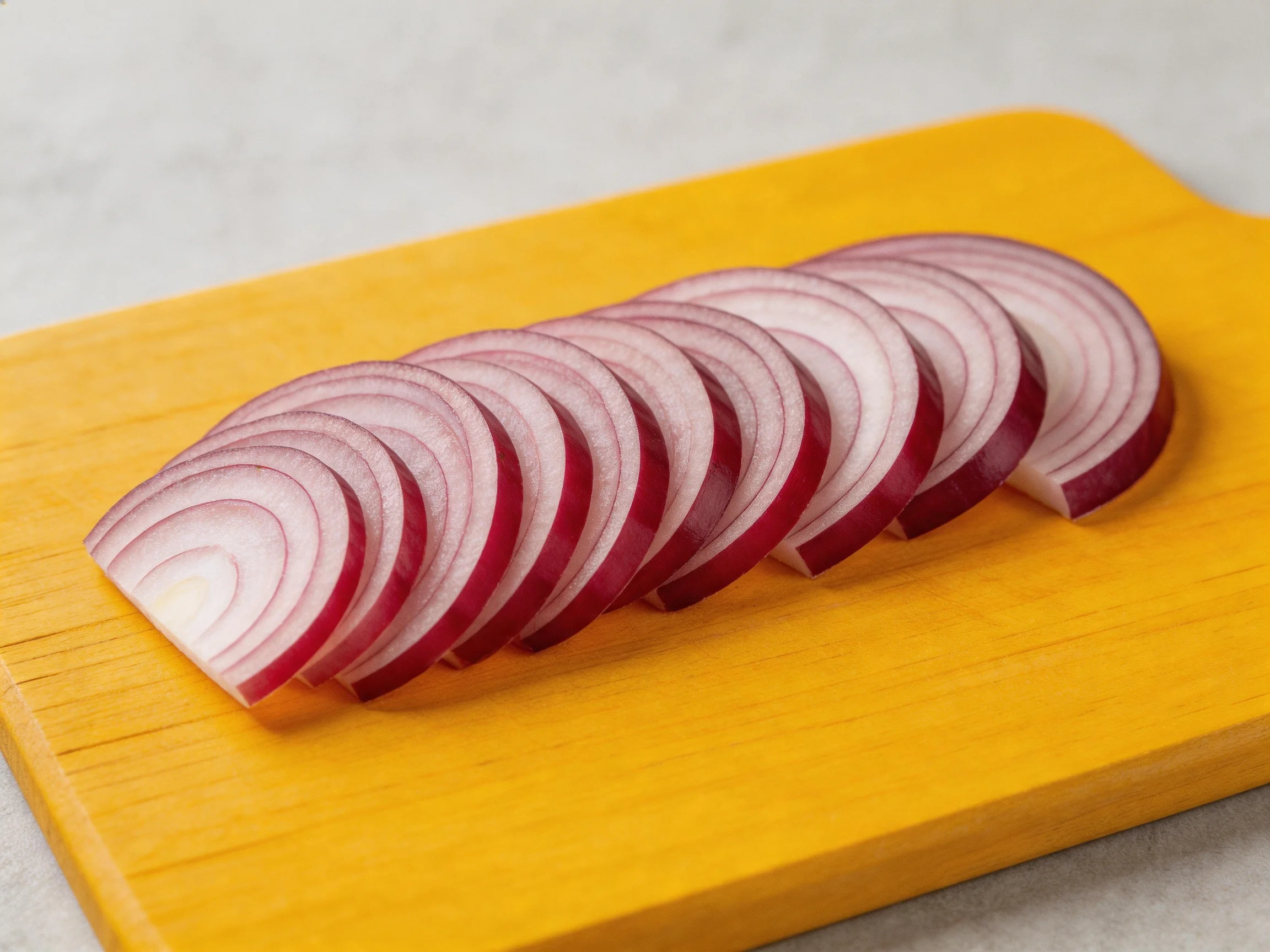 Sliced red onion rings arranged on a bright yellow wooden cutting board