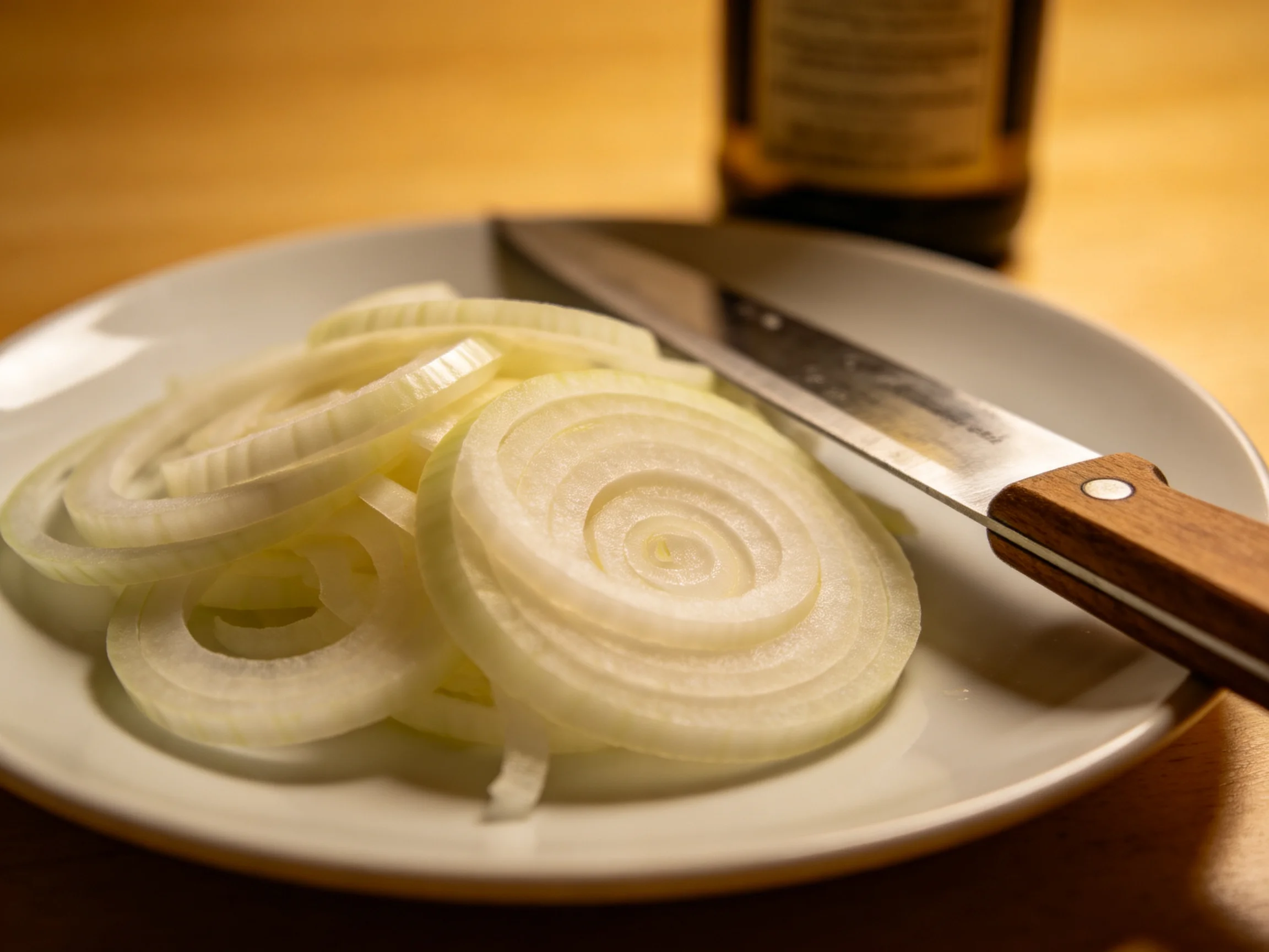 Sliced white onions on a plate with a wooden-handled knife