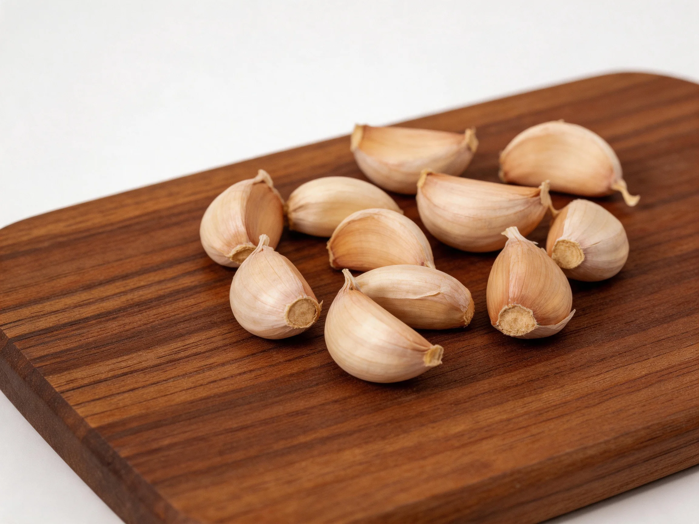 Ten garlic cloves arranged on a polished brown wooden cutting board