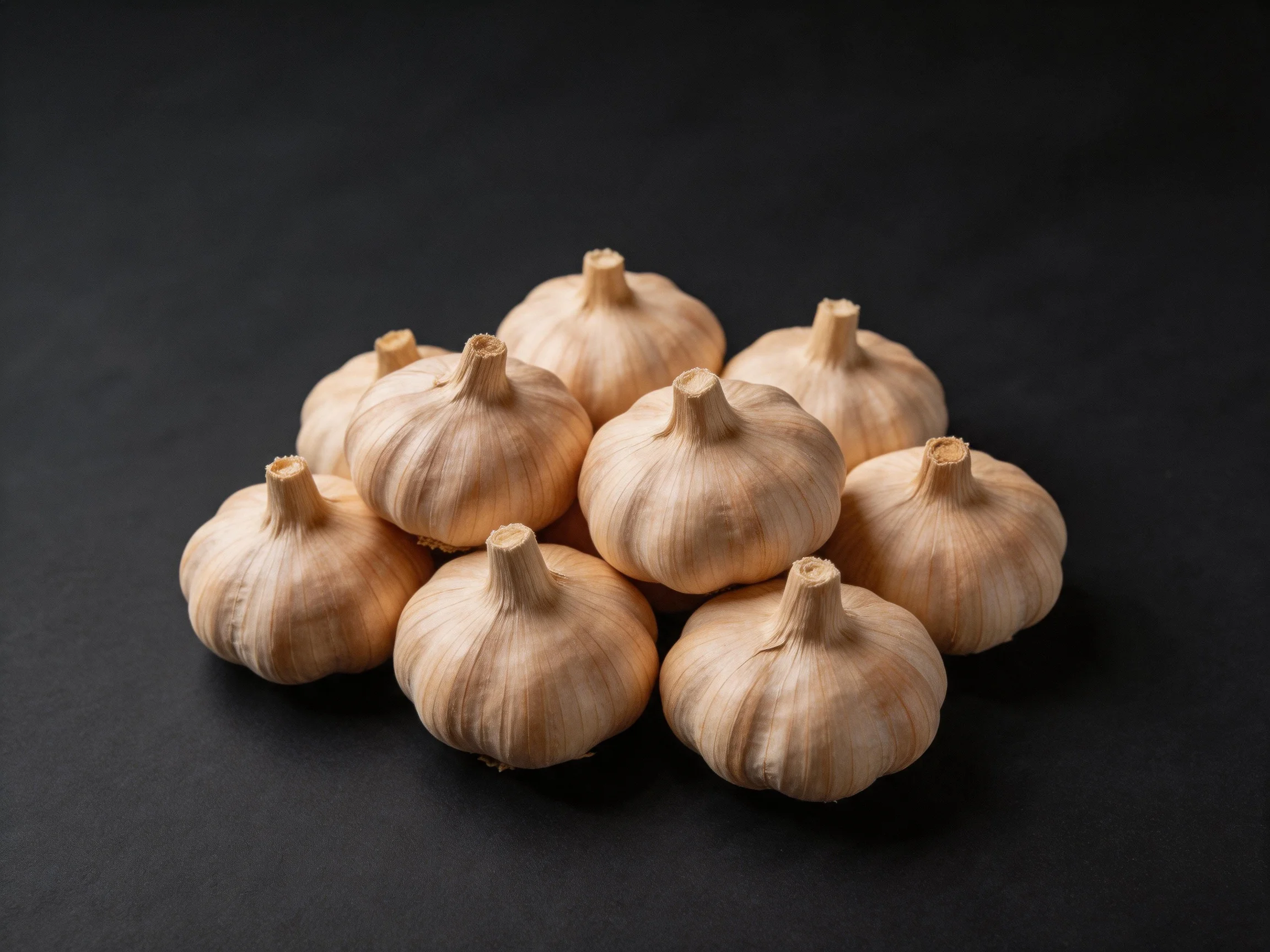 Ten pale garlic bulbs clustered on a black surface