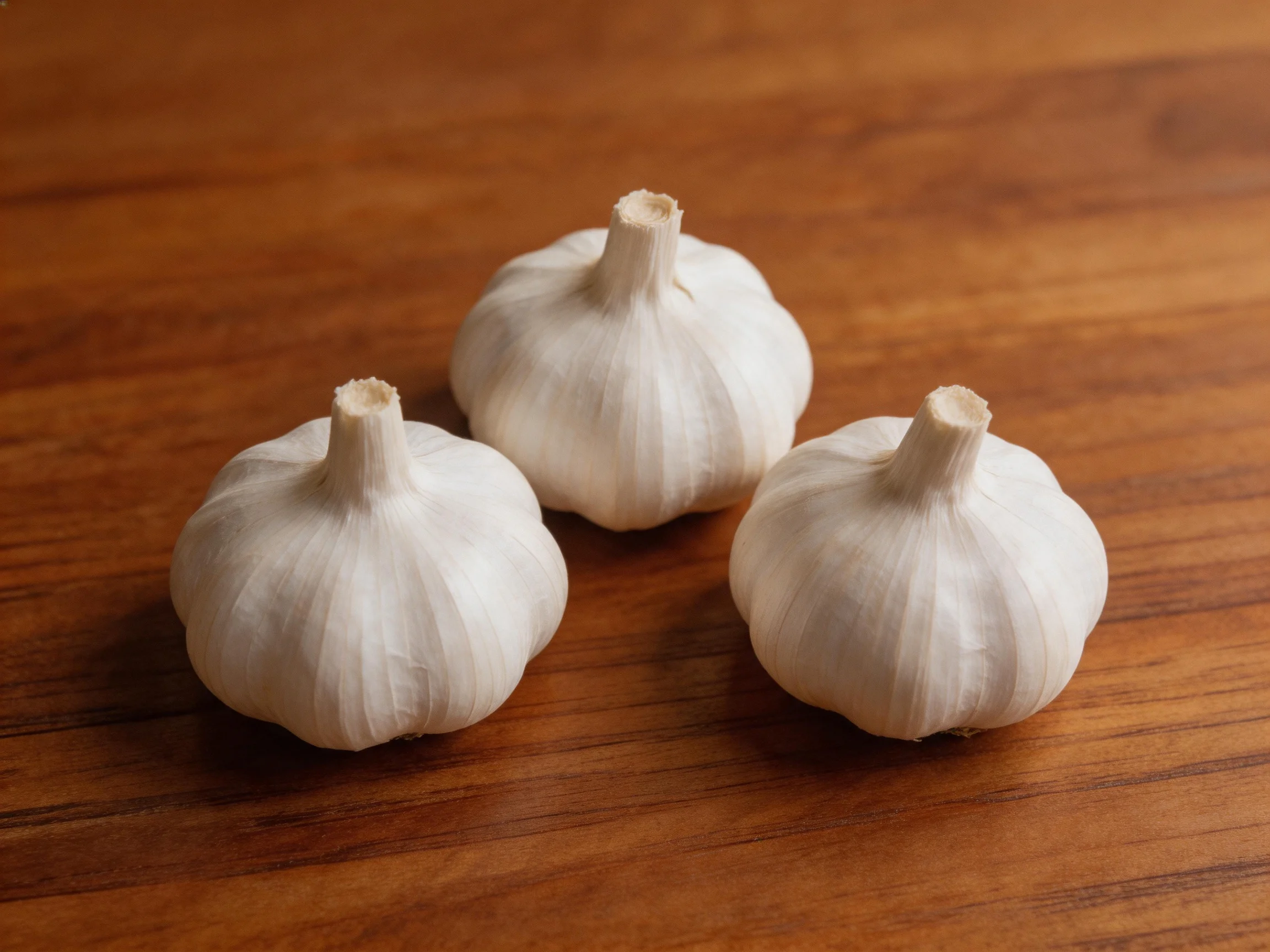 Three fresh garlic bulbs arranged on a polished wooden surface