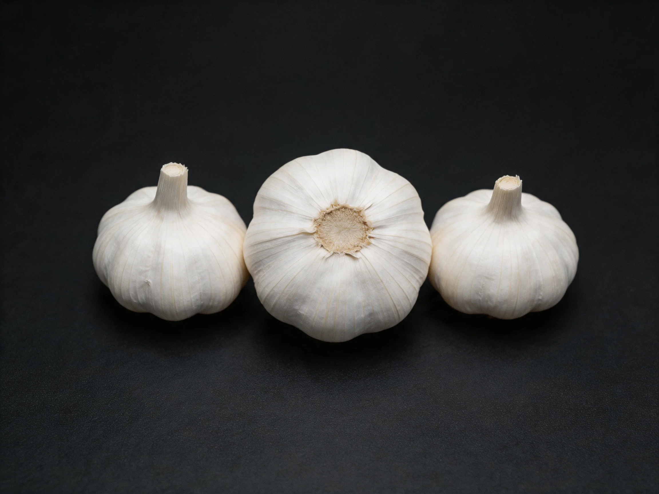 Three garlic bulbs arranged on a dark surface