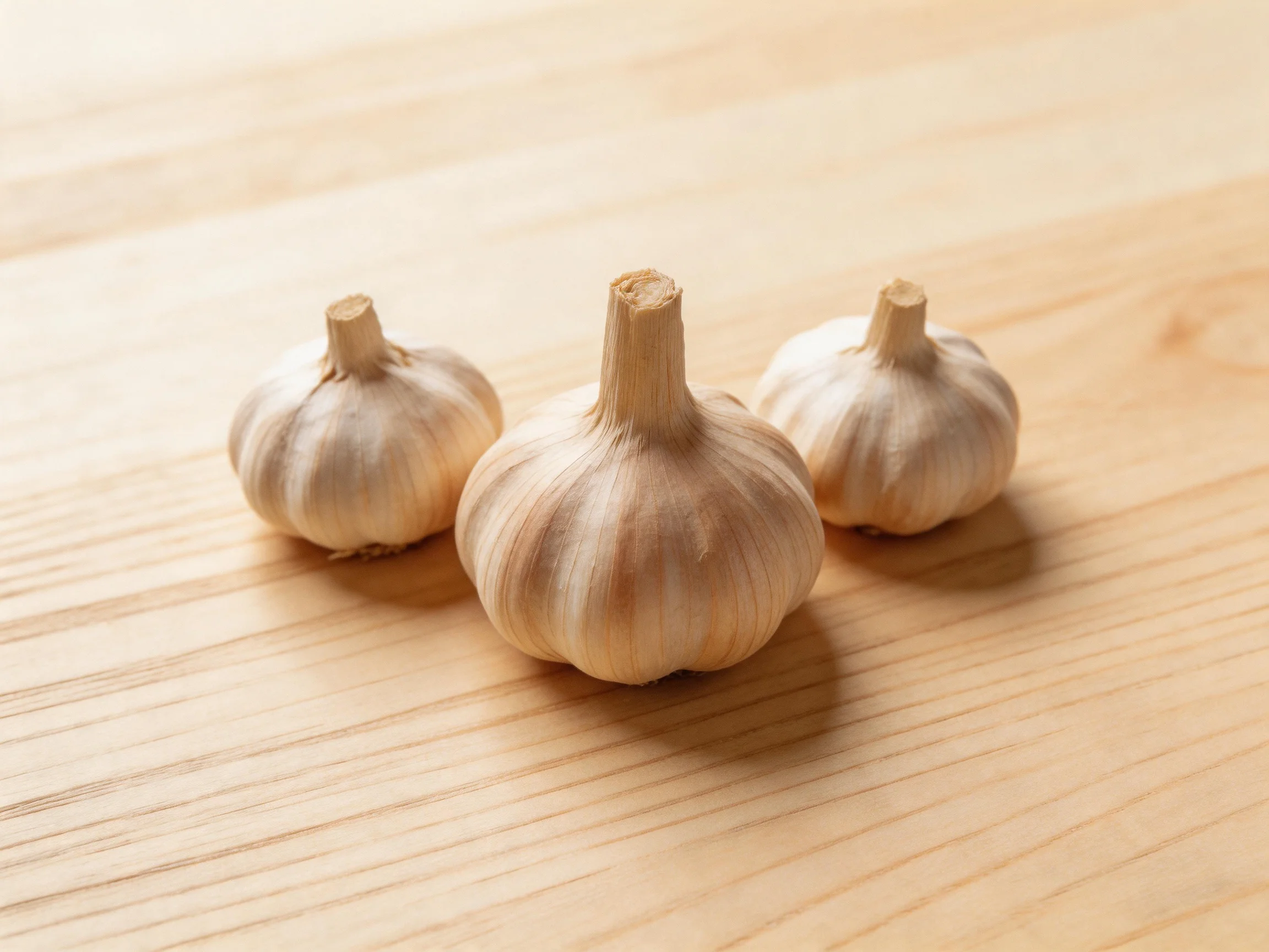 Three garlic bulbs with light brown skins on a wooden surface