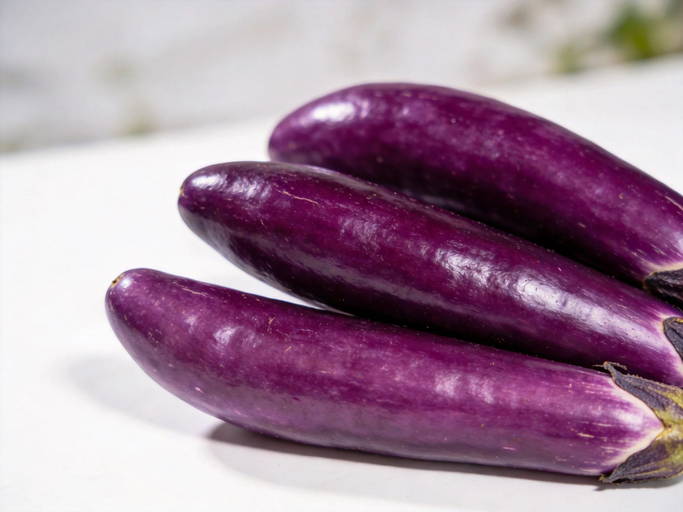 Three glossy purple eggplants clustered on a white surface