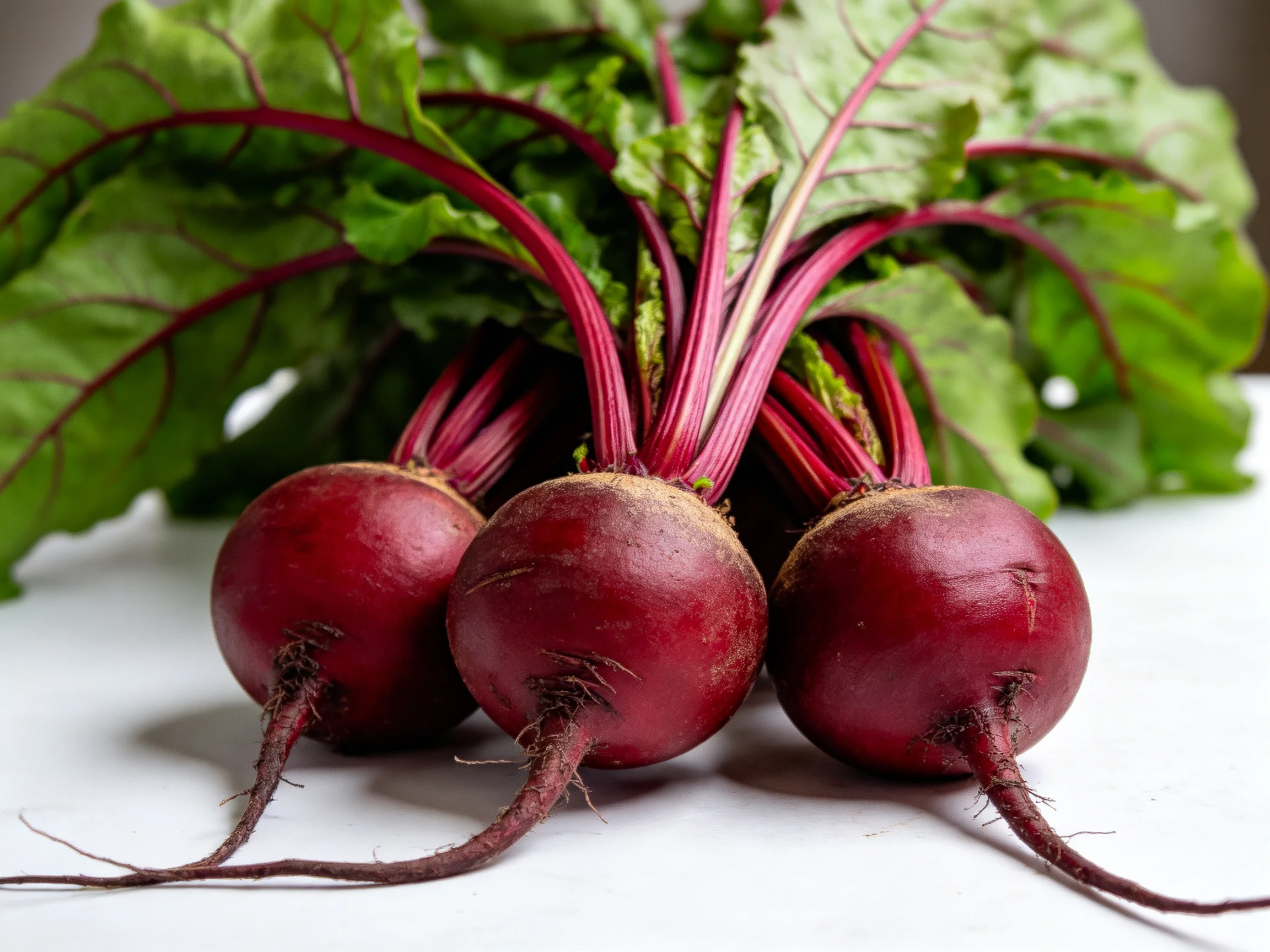 Three glossy red beetroots with leafy green foliage grouped together