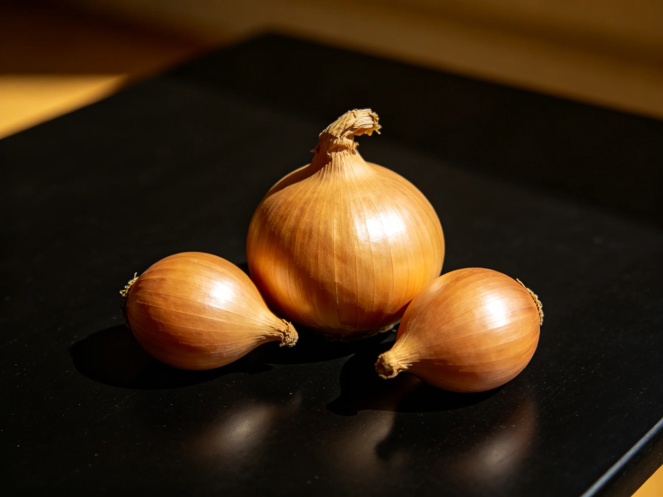 Three golden-brown onions arranged on a glossy black surface